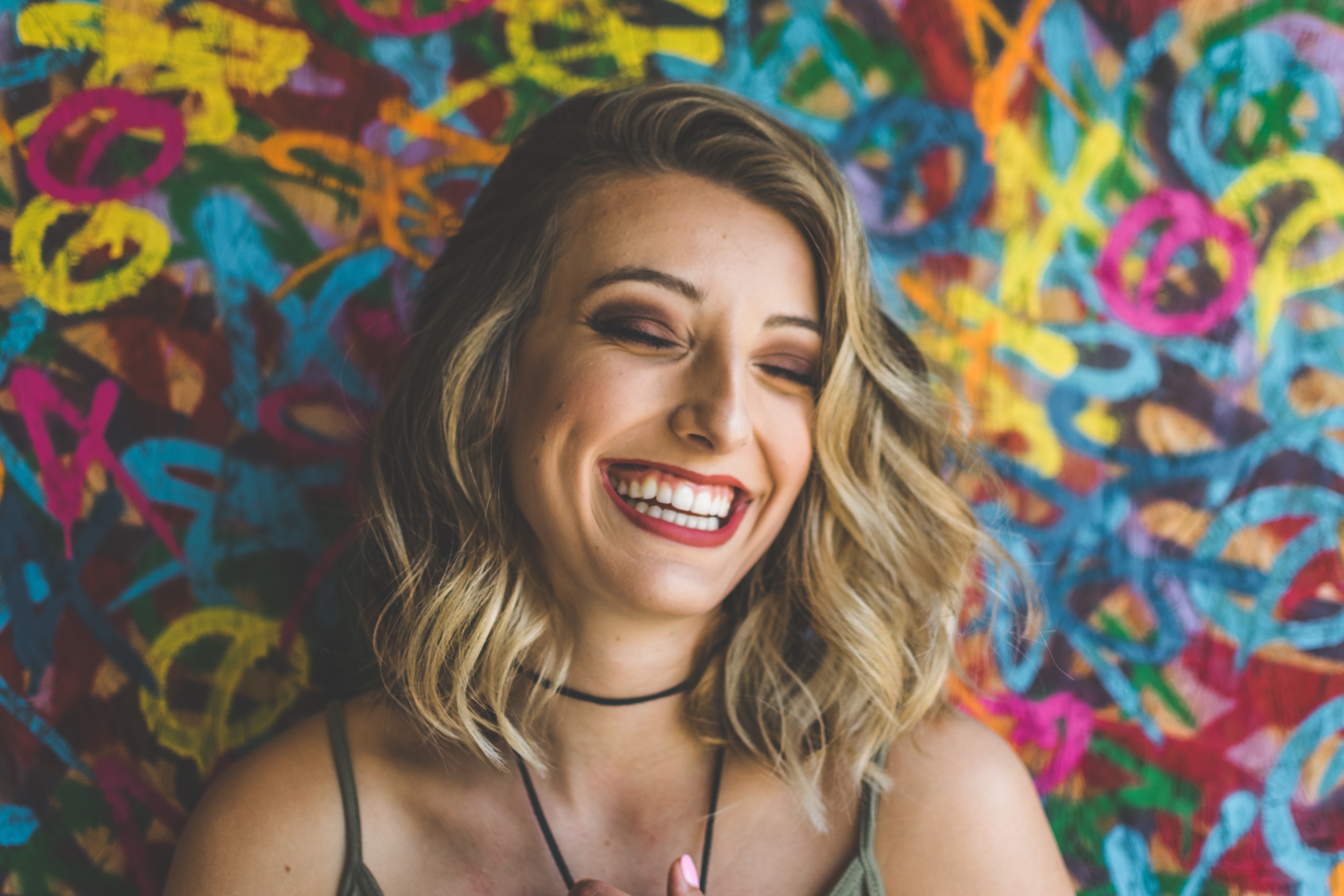 Woman laughing in front of colorful graffiti wall HD Wallpaper