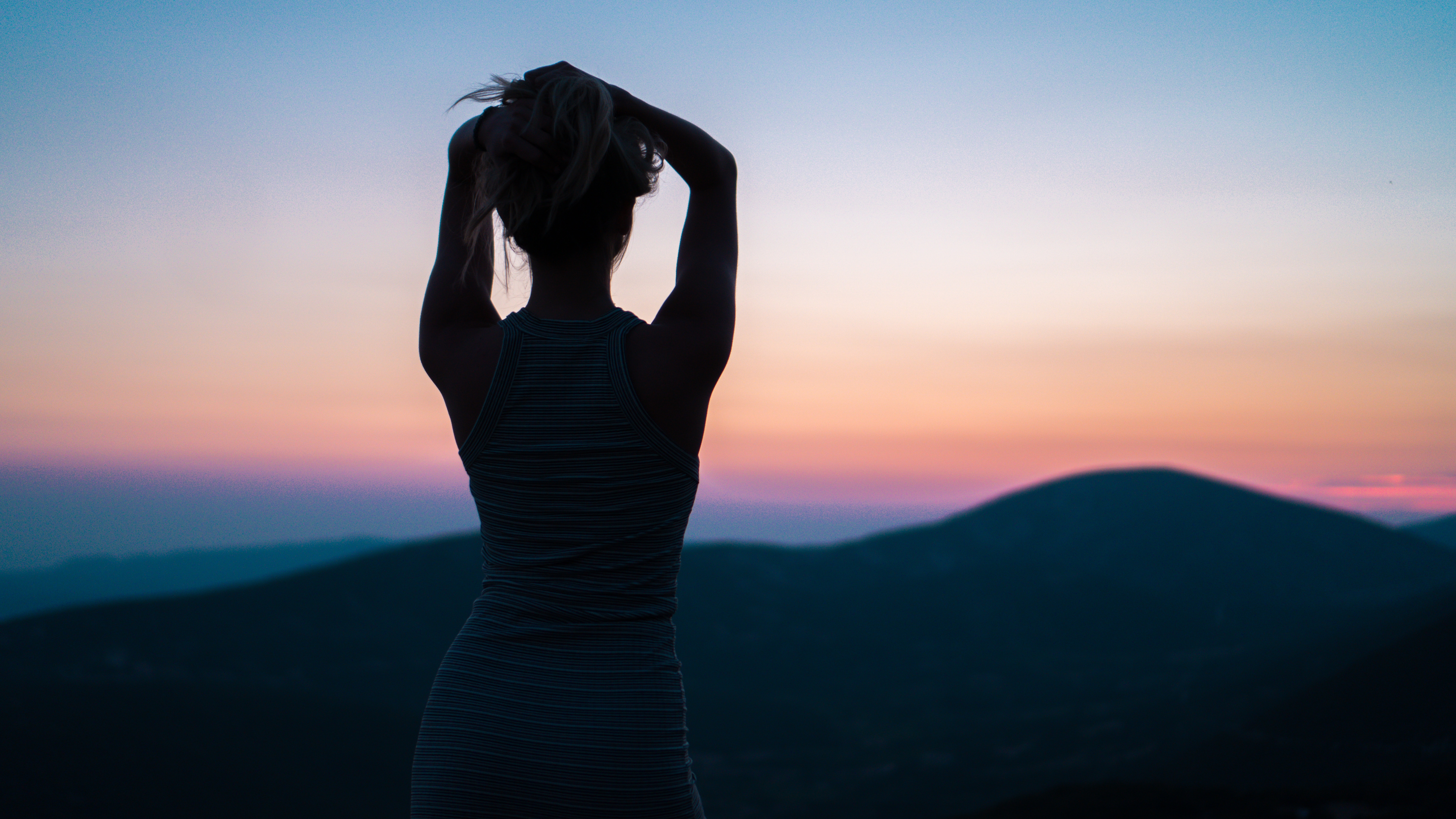 Woman silhouetted against a colorful sunset over mountains HD Wallpaper