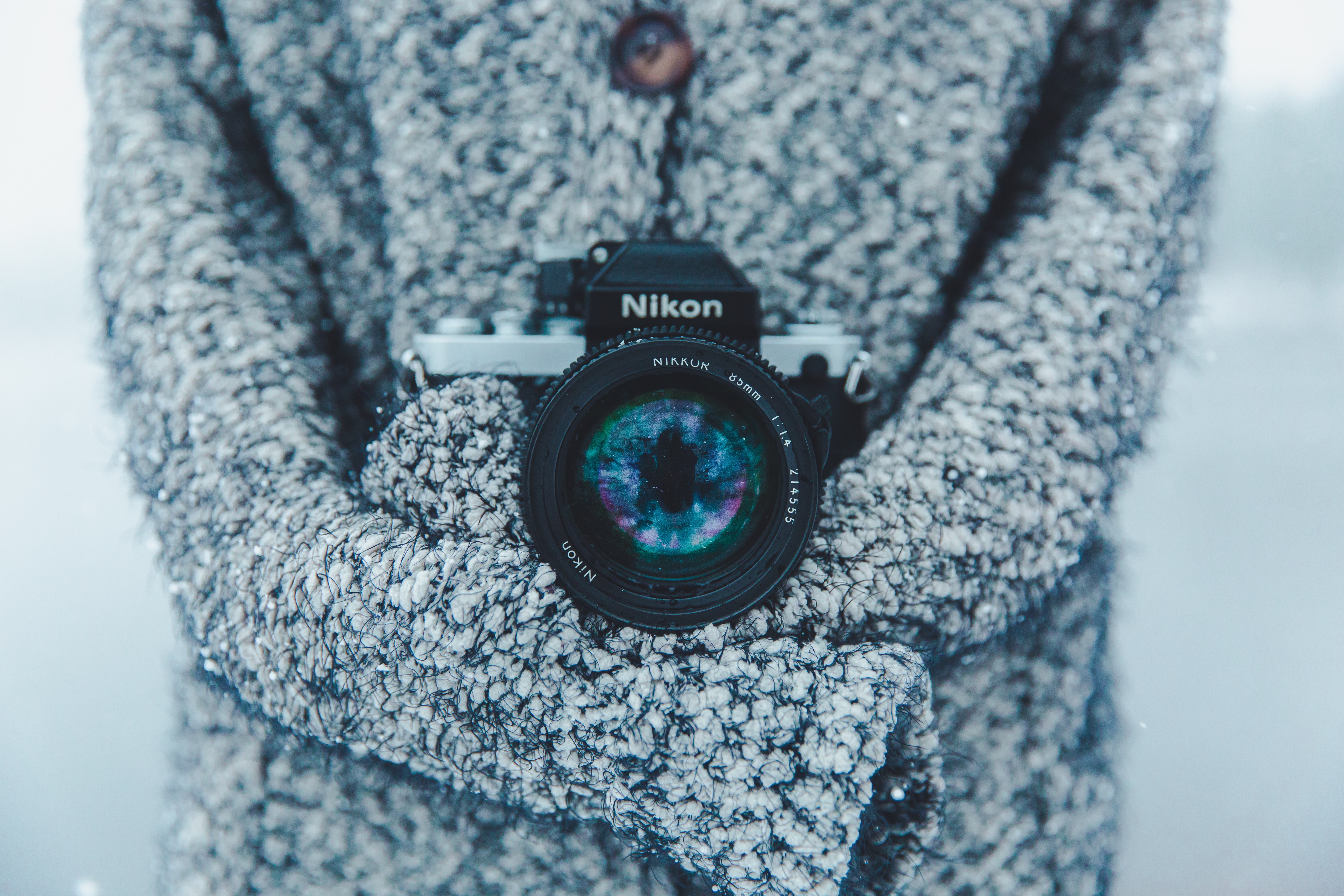 Person holding a vintage Nikon camera in a snowy forest HD Wallpaper