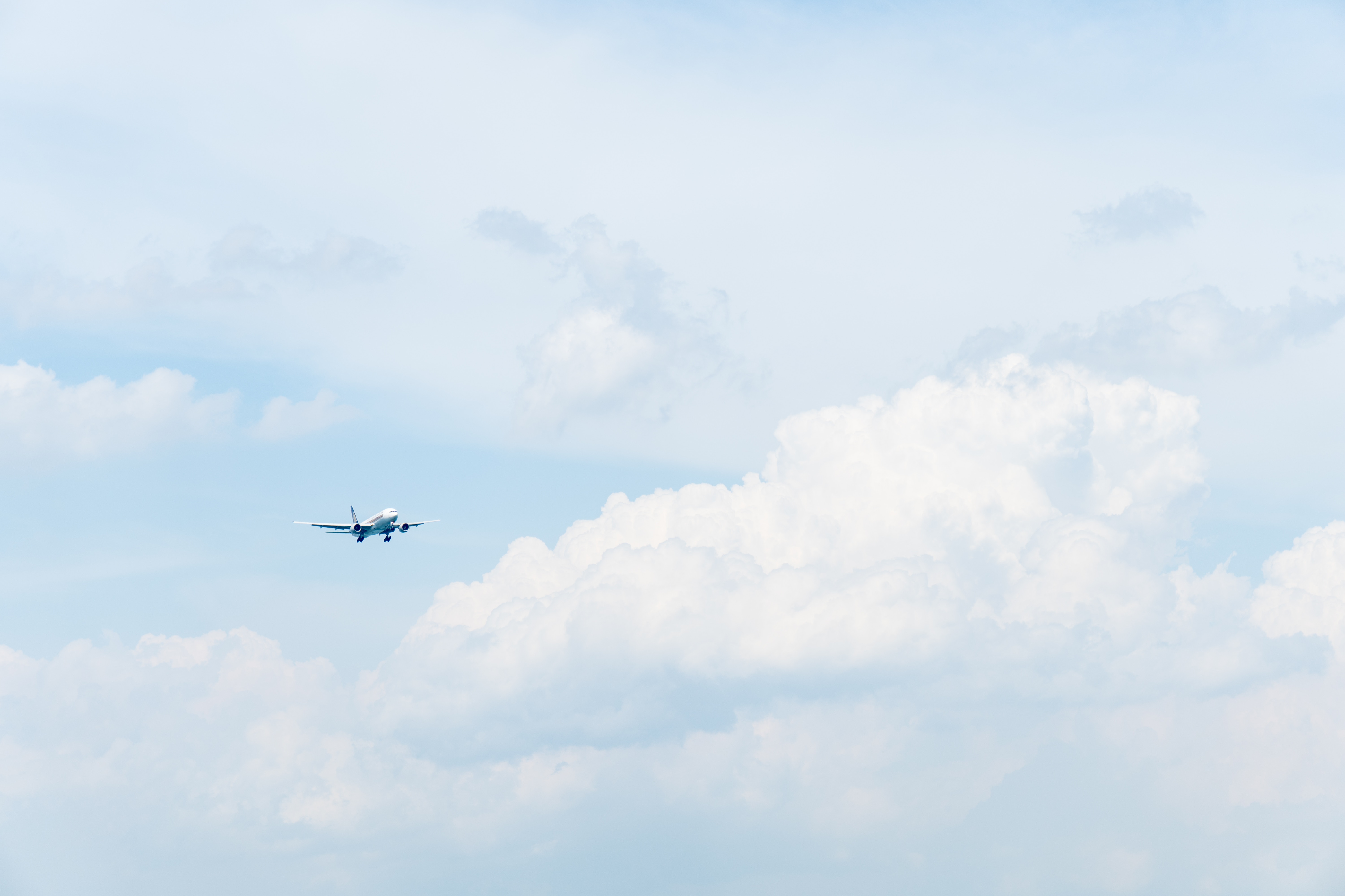 Airplane flying in a pastel blue sky with clouds HD Wallpaper