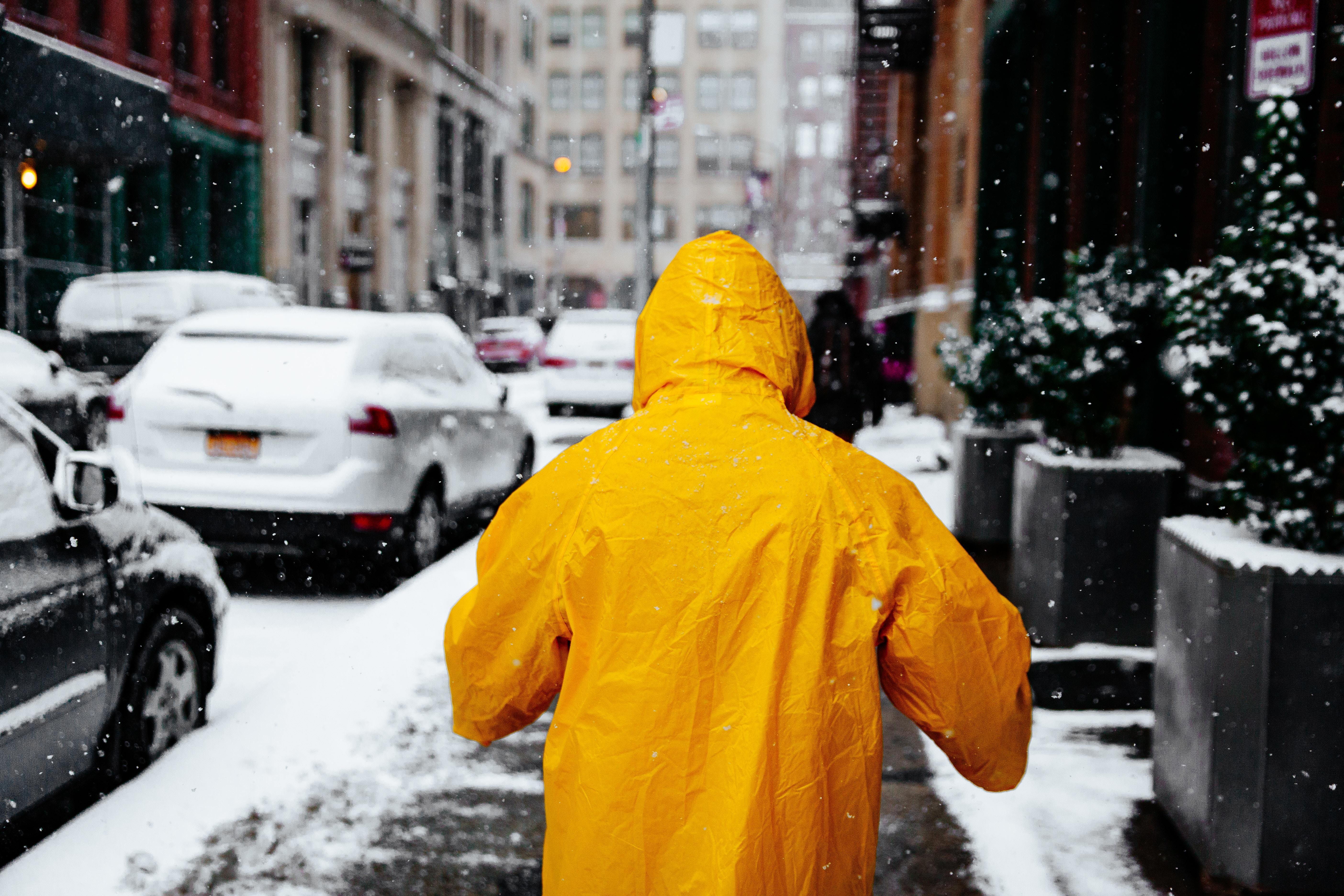 Person in yellow raincoat walking in snowy New York City HD Wallpaper