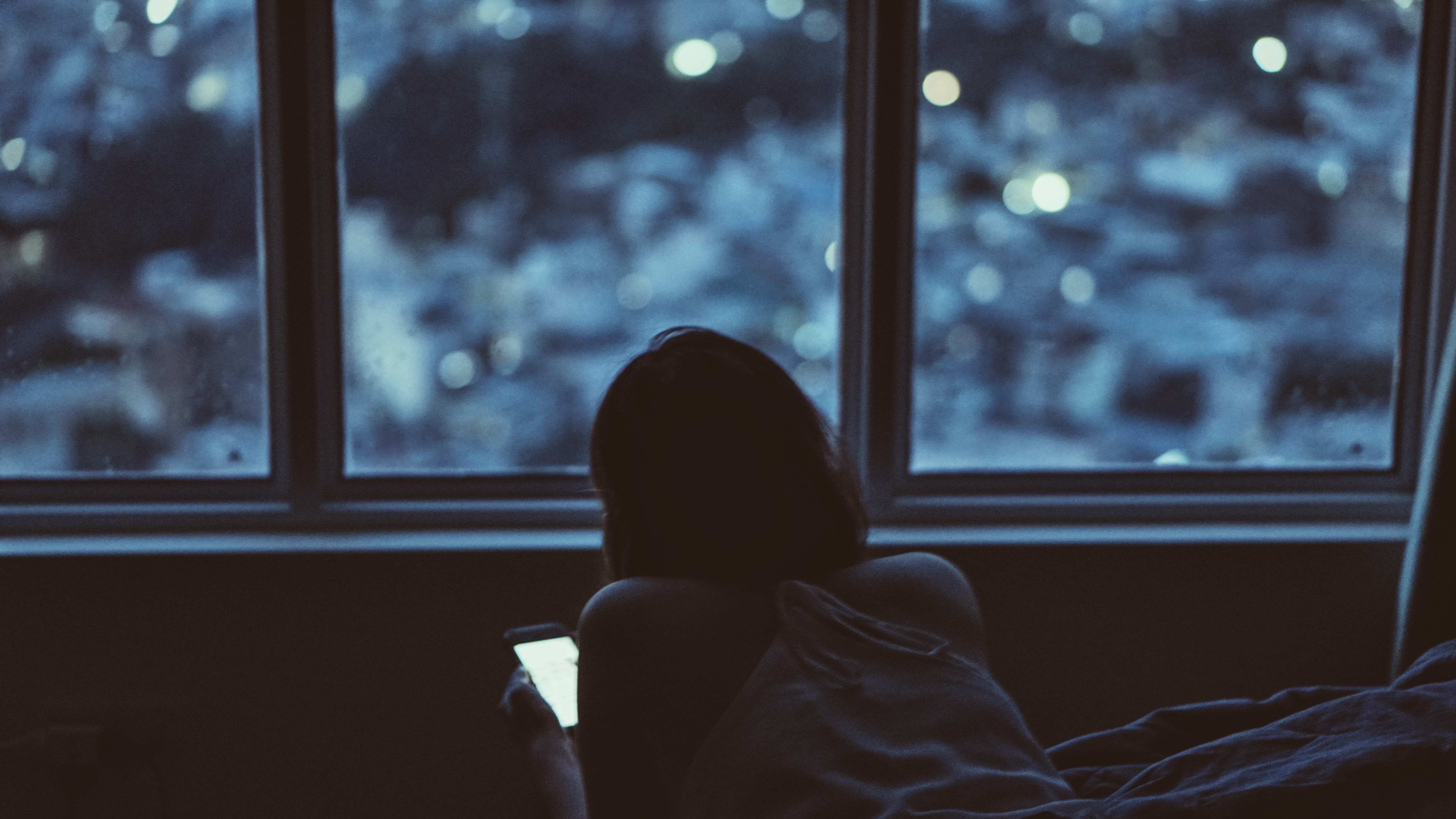 Woman looking at phone by the window at night HD Wallpaper