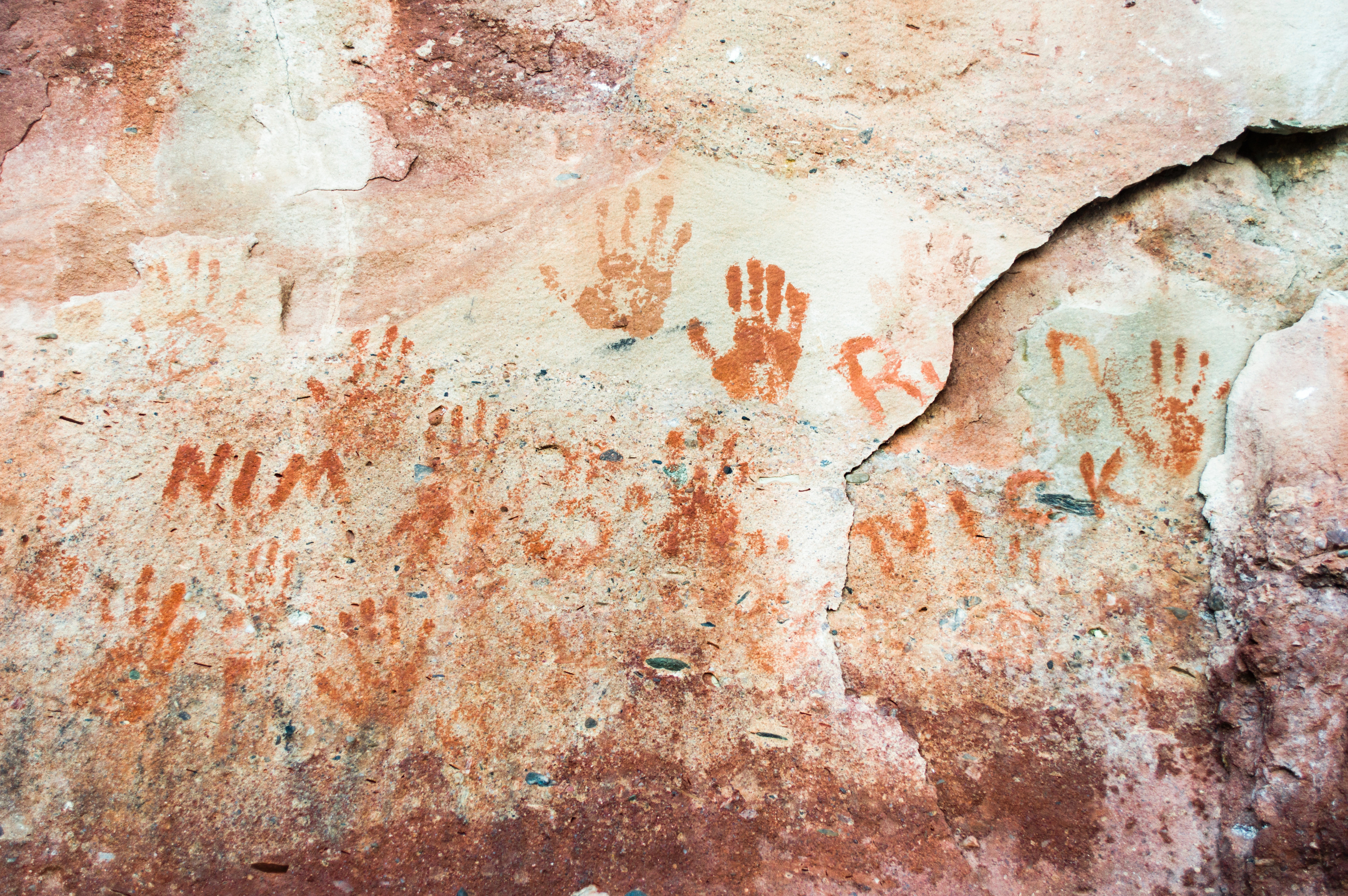 Ancient handprints painted on a textured rock wall HD Wallpaper