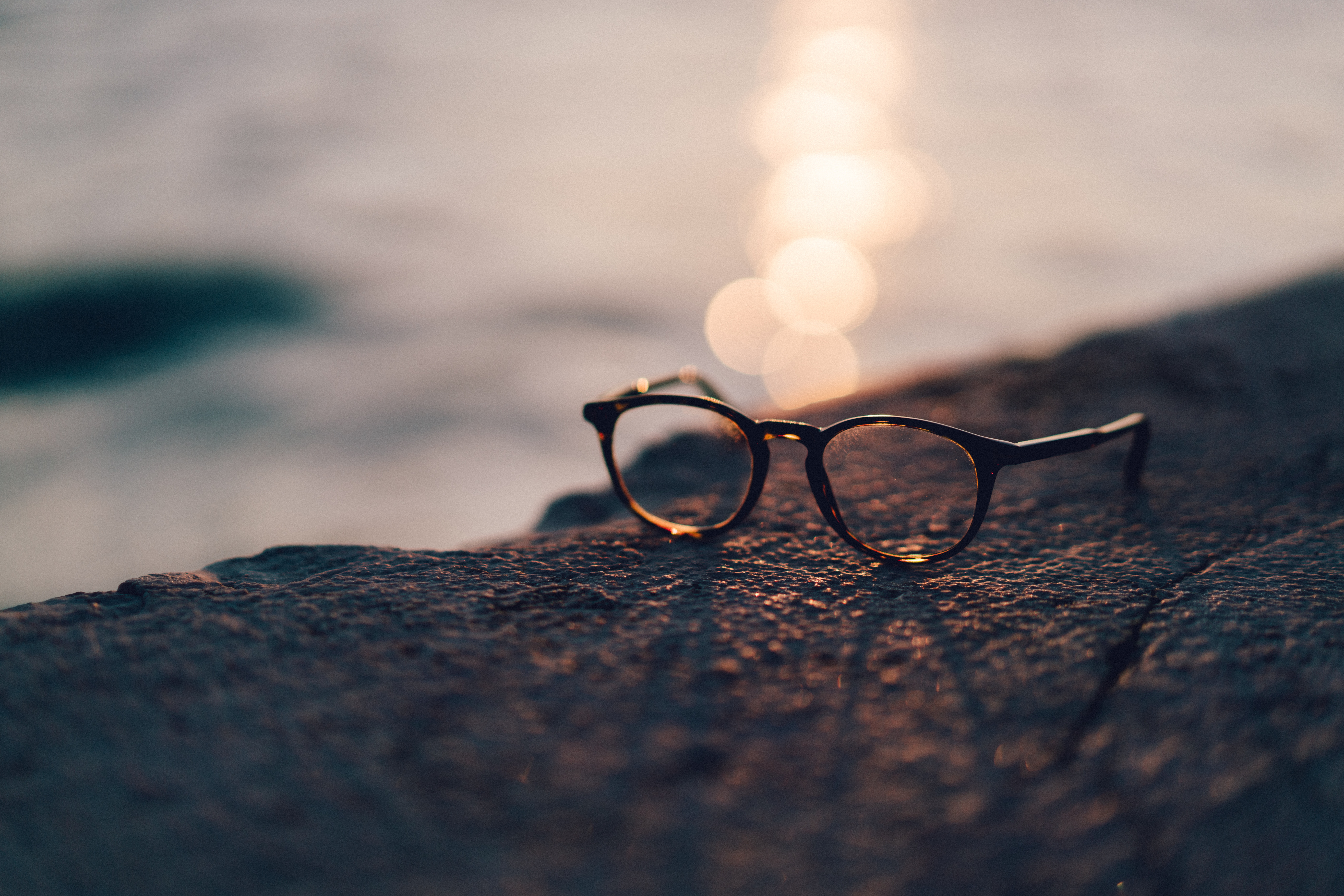 Eyeglasses on a rock by the water at sunset HD Wallpaper