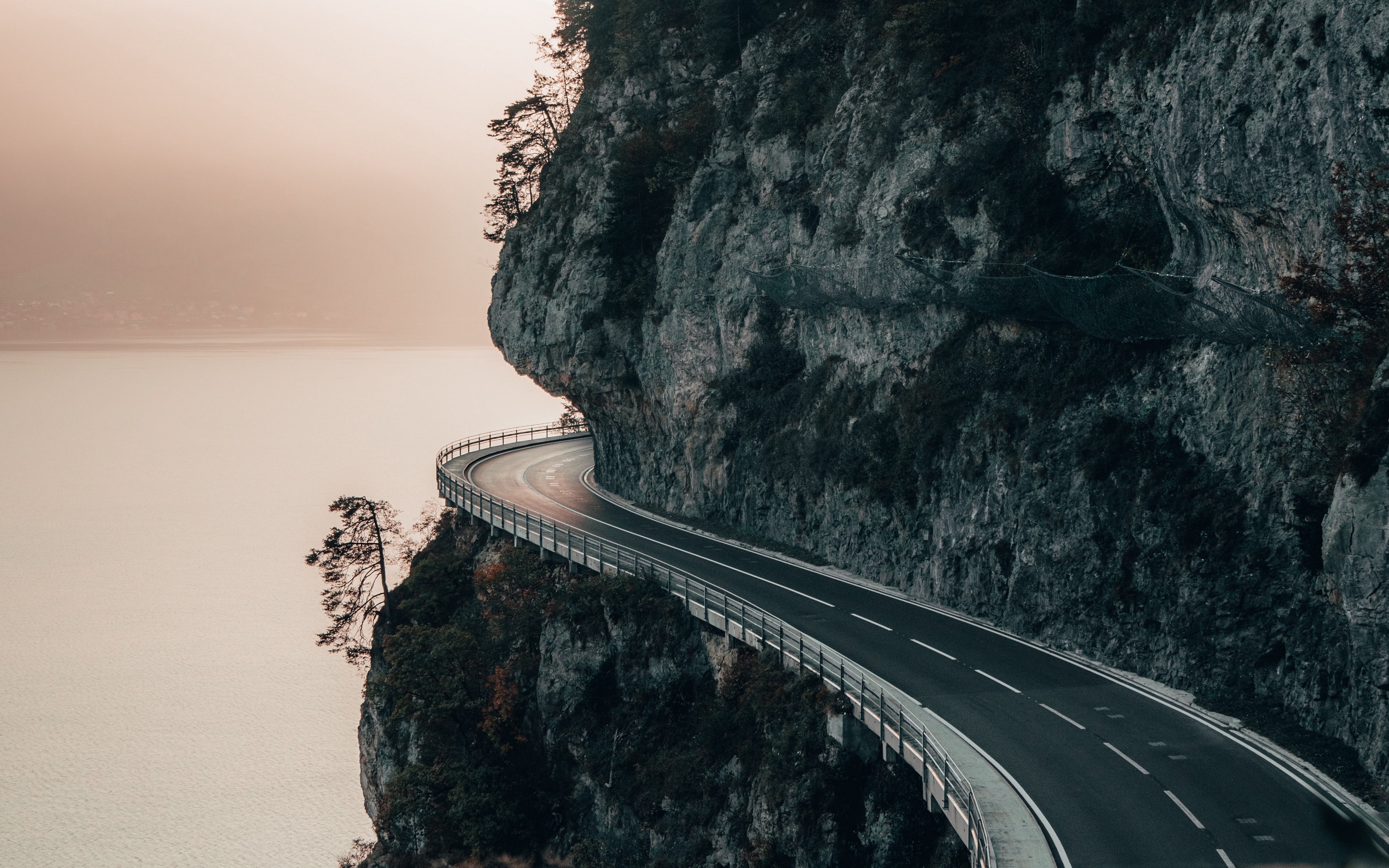 Road carved into a cliff overlooking a body of water HD Wallpaper