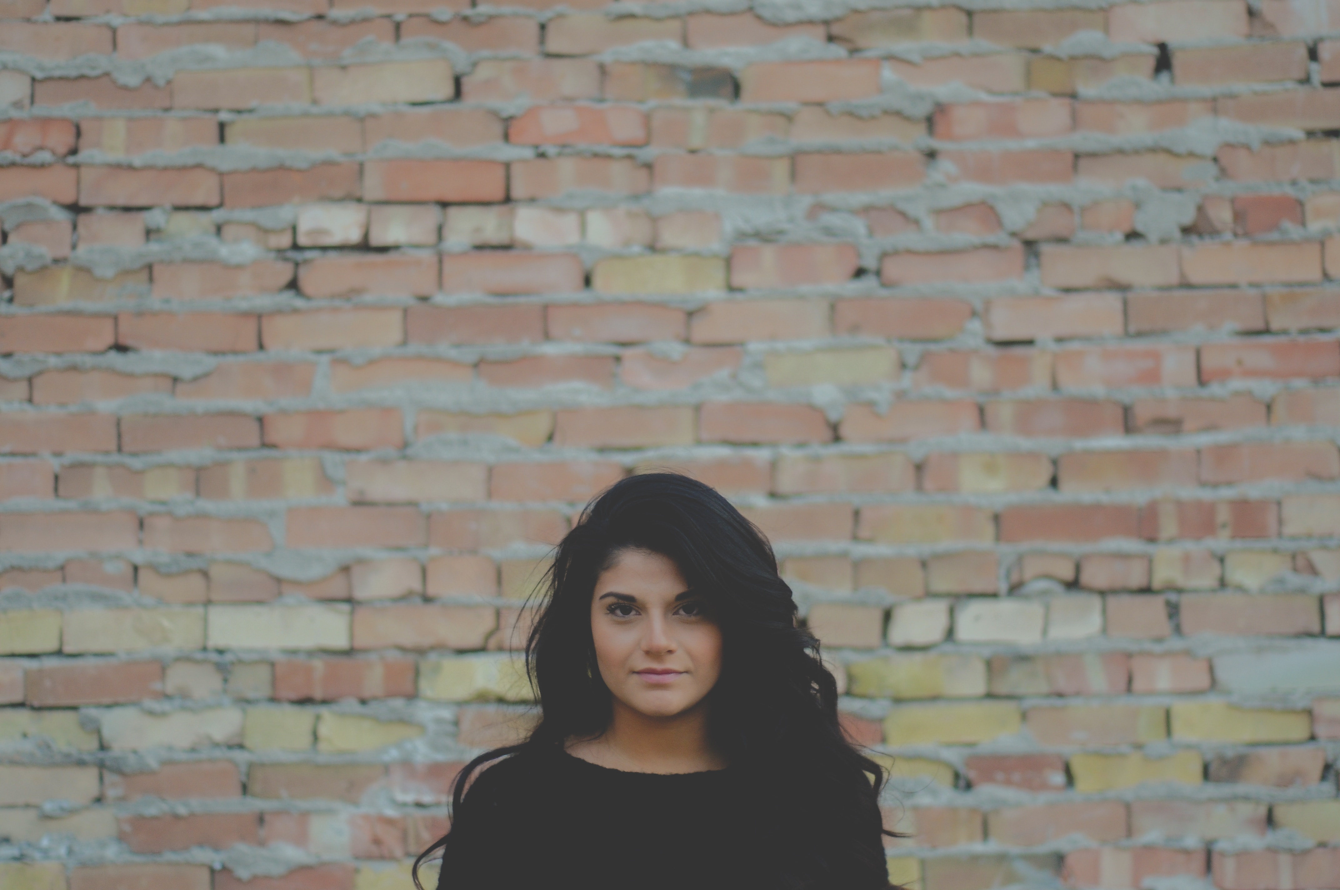 Woman with long black hair in front of a brick wall HD Wallpaper