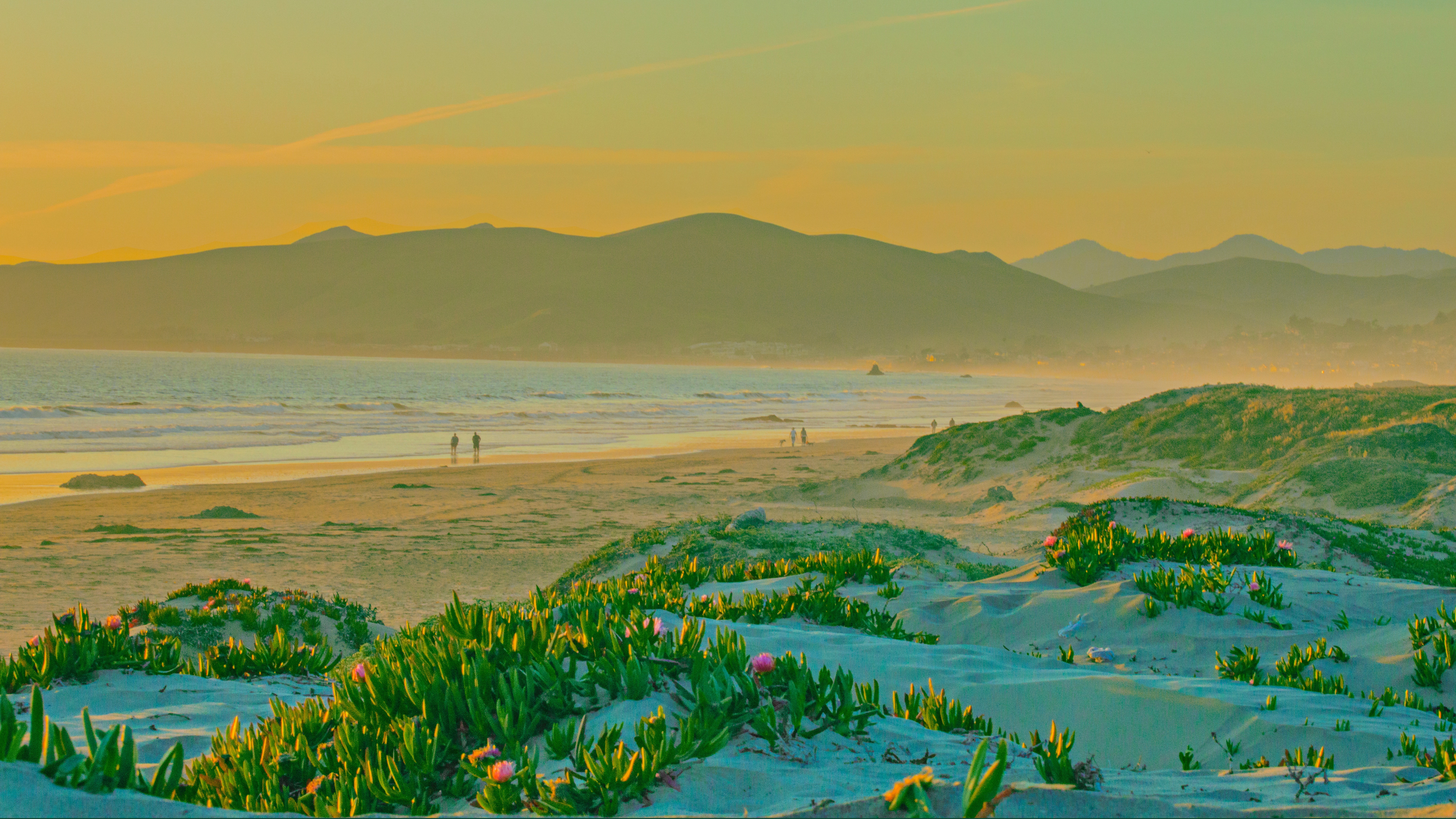 Golden hour sunset over a sandy beach with dunes and mountains HD Wallpaper