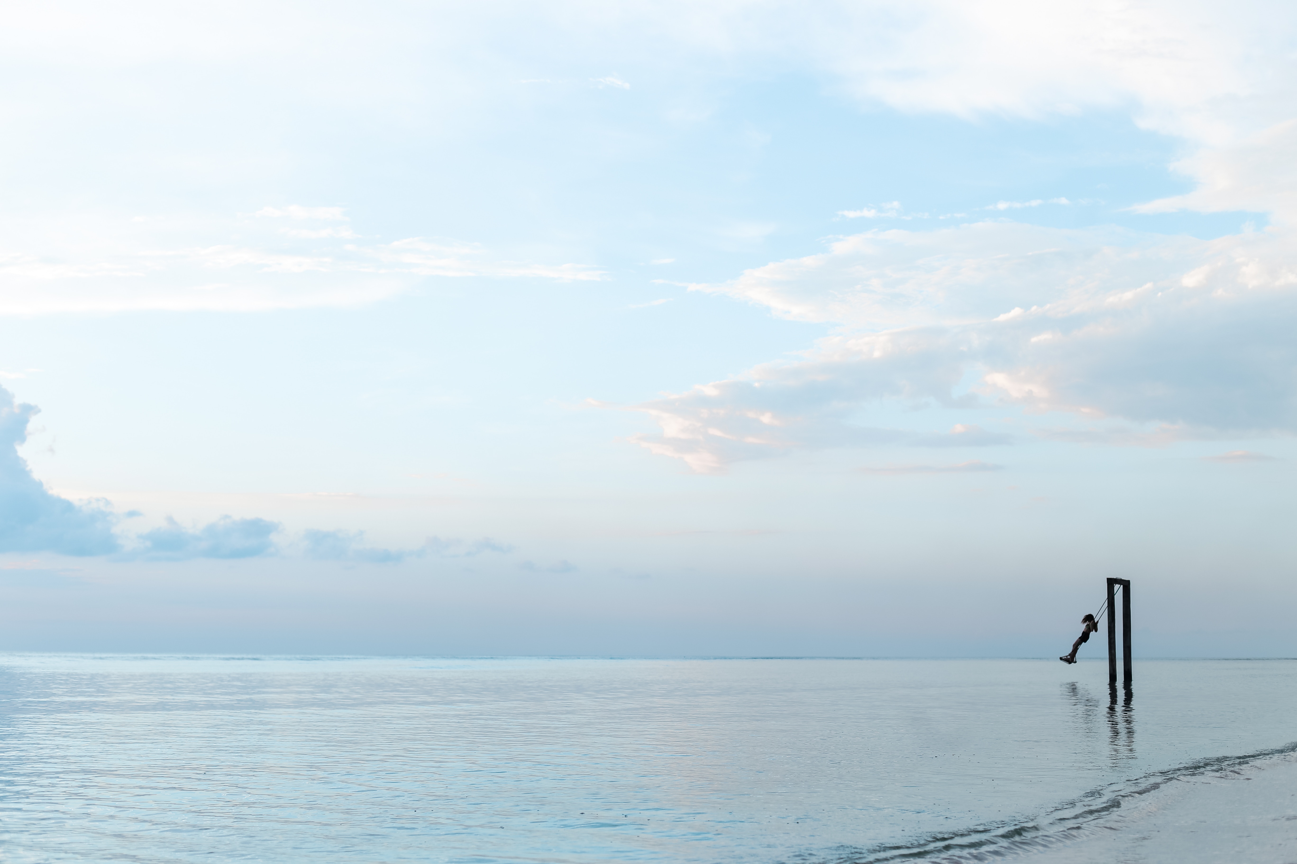 Person on a swing in the calm sea under a cloudy sky HD Wallpaper