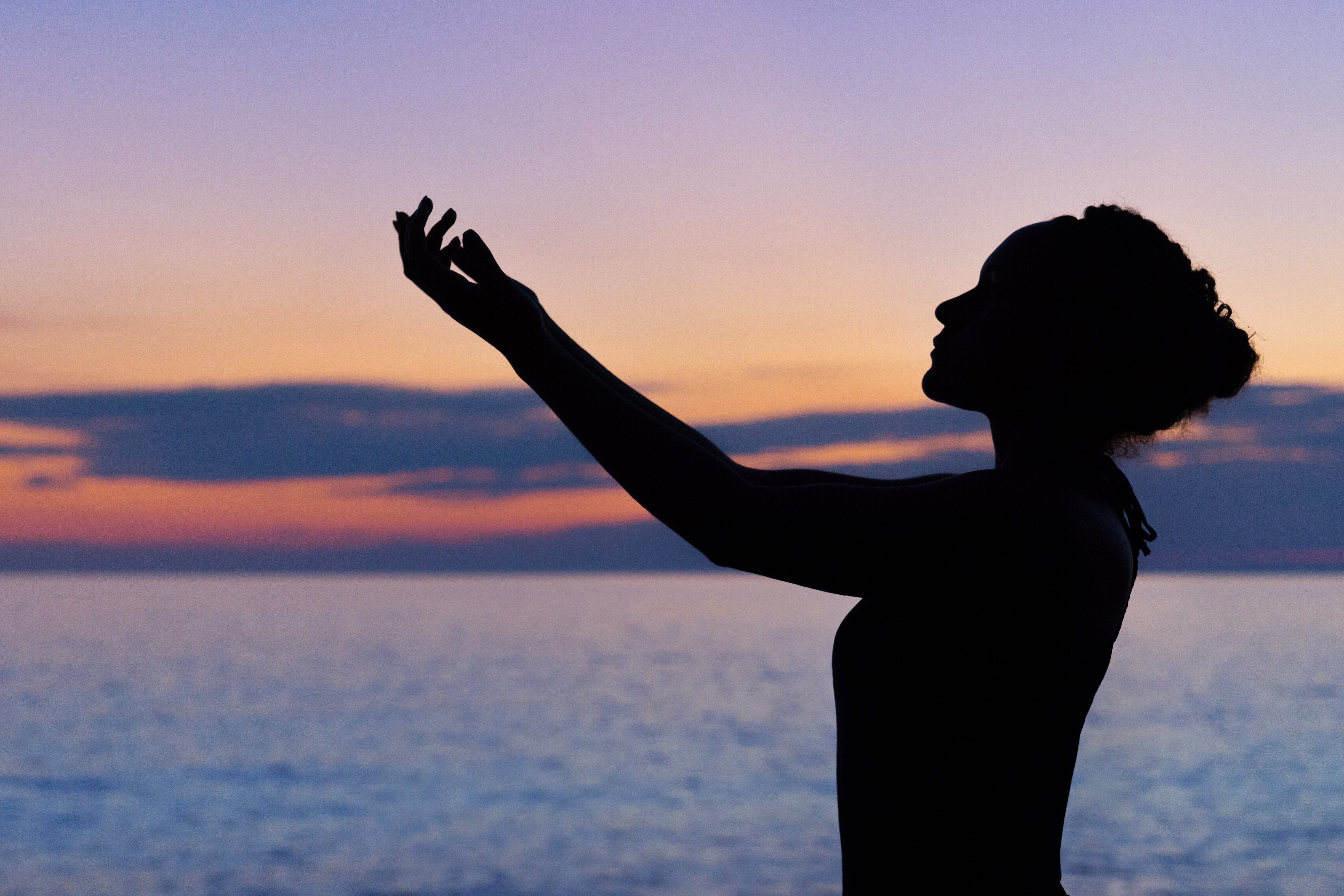Silhouette of a woman with arms raised at sunset over the ocean HD Wallpaper