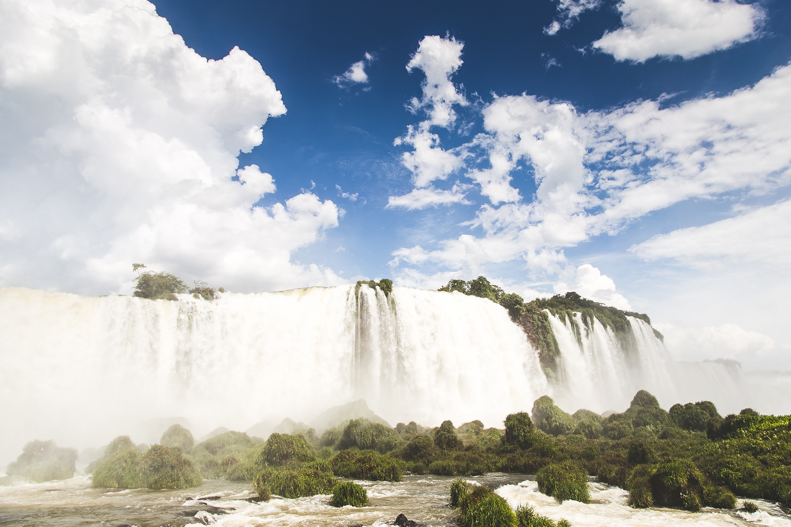 Misty waterfall with lush green vegetation and blue sky HD Wallpaper