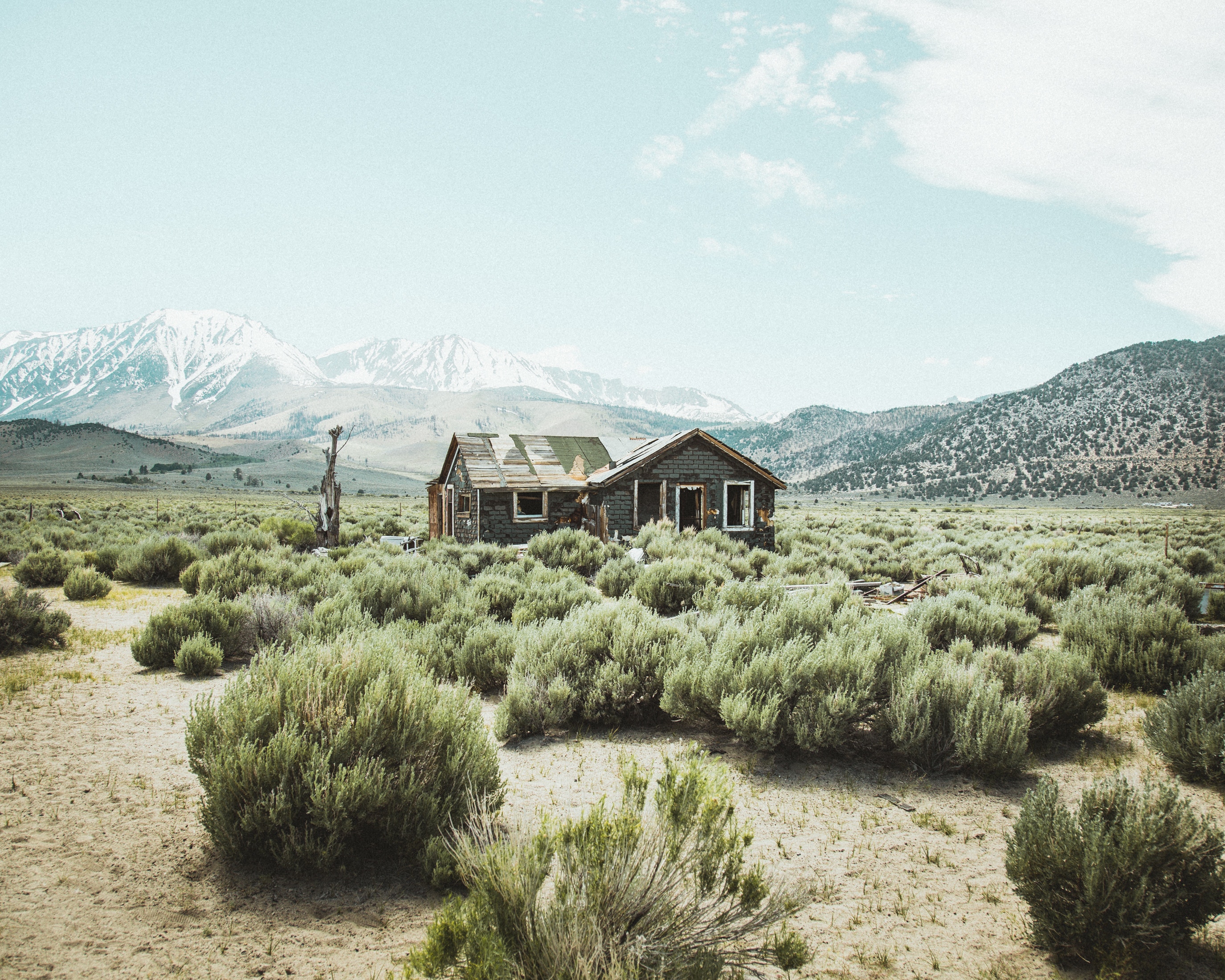 Abandoned cabin in a desert valley with snowy mountains HD Wallpaper