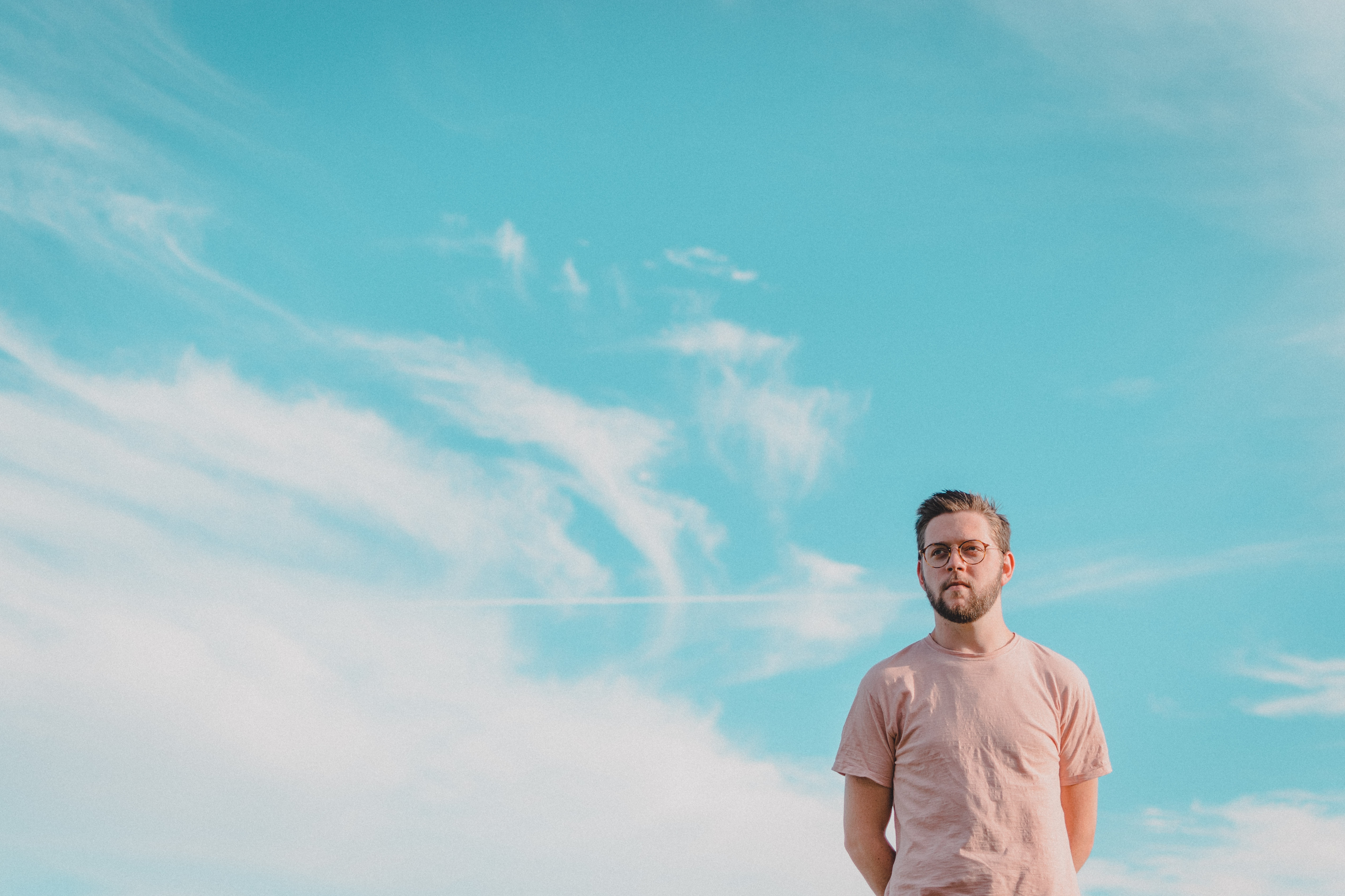 Man with beard and glasses in a pink t-shirt against blue sky HD Wallpaper