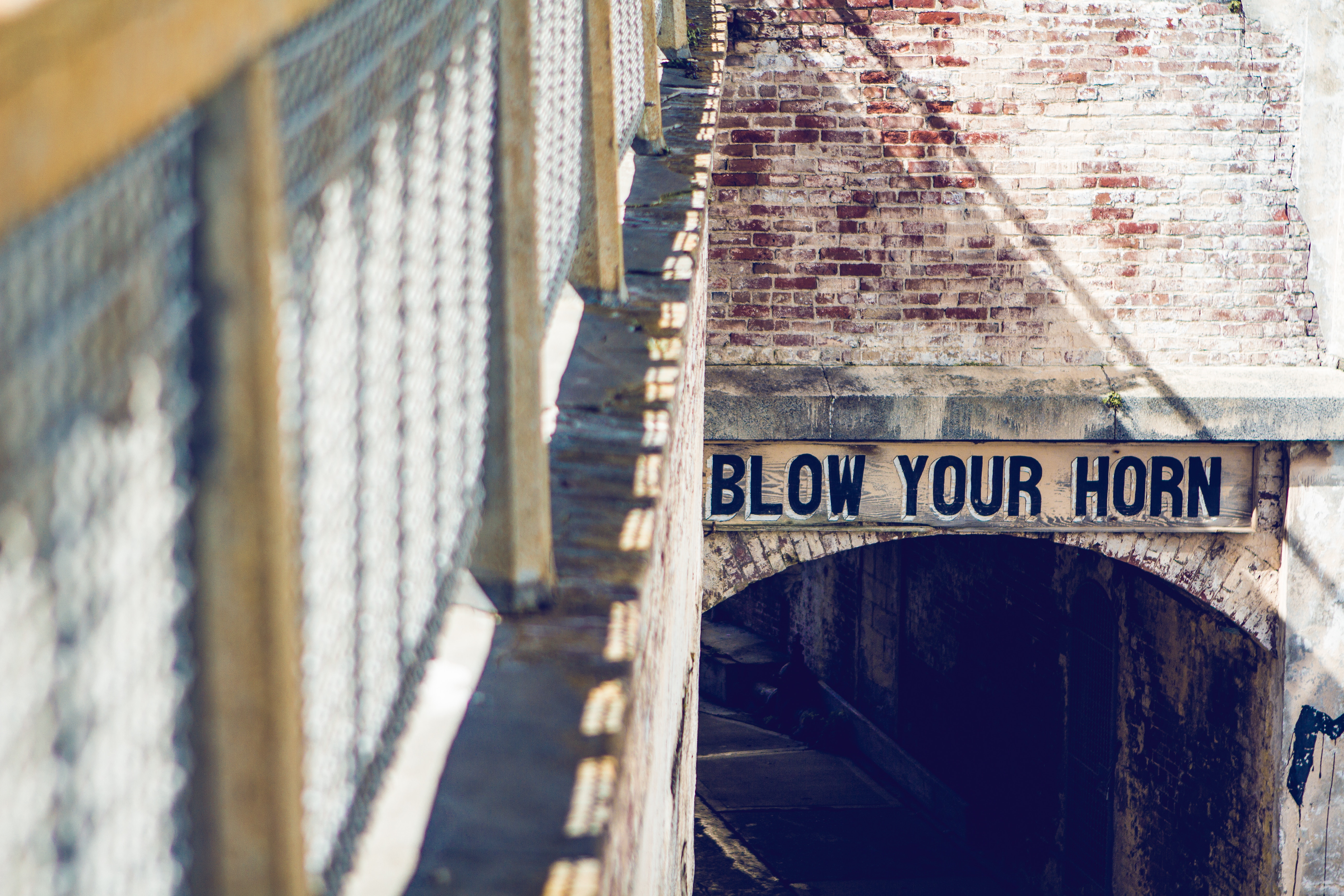 Sign that says "BLOW YOUR HORN" over an archway HD Wallpaper