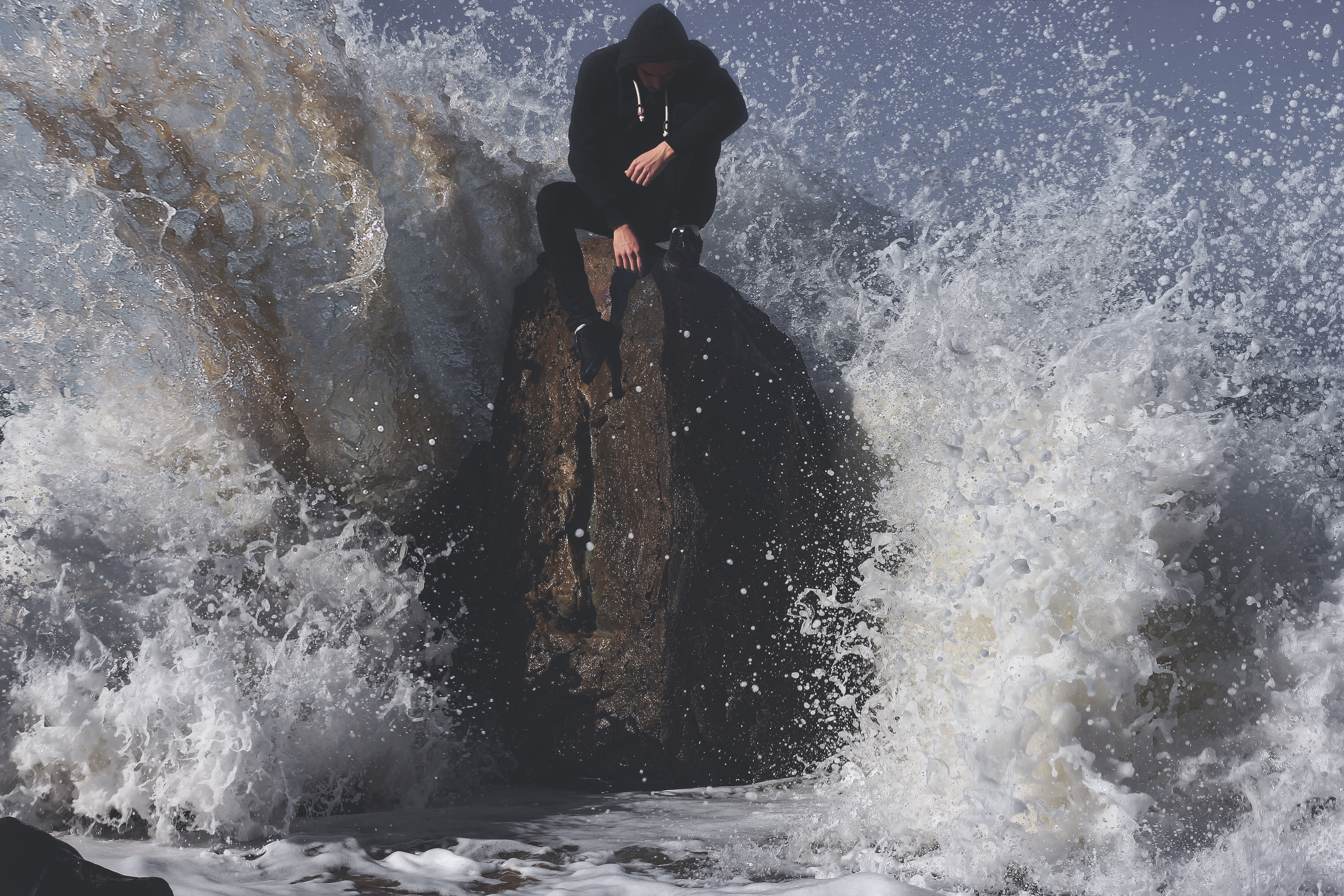 Man in hoodie sitting on a rock in the ocean HD Wallpaper