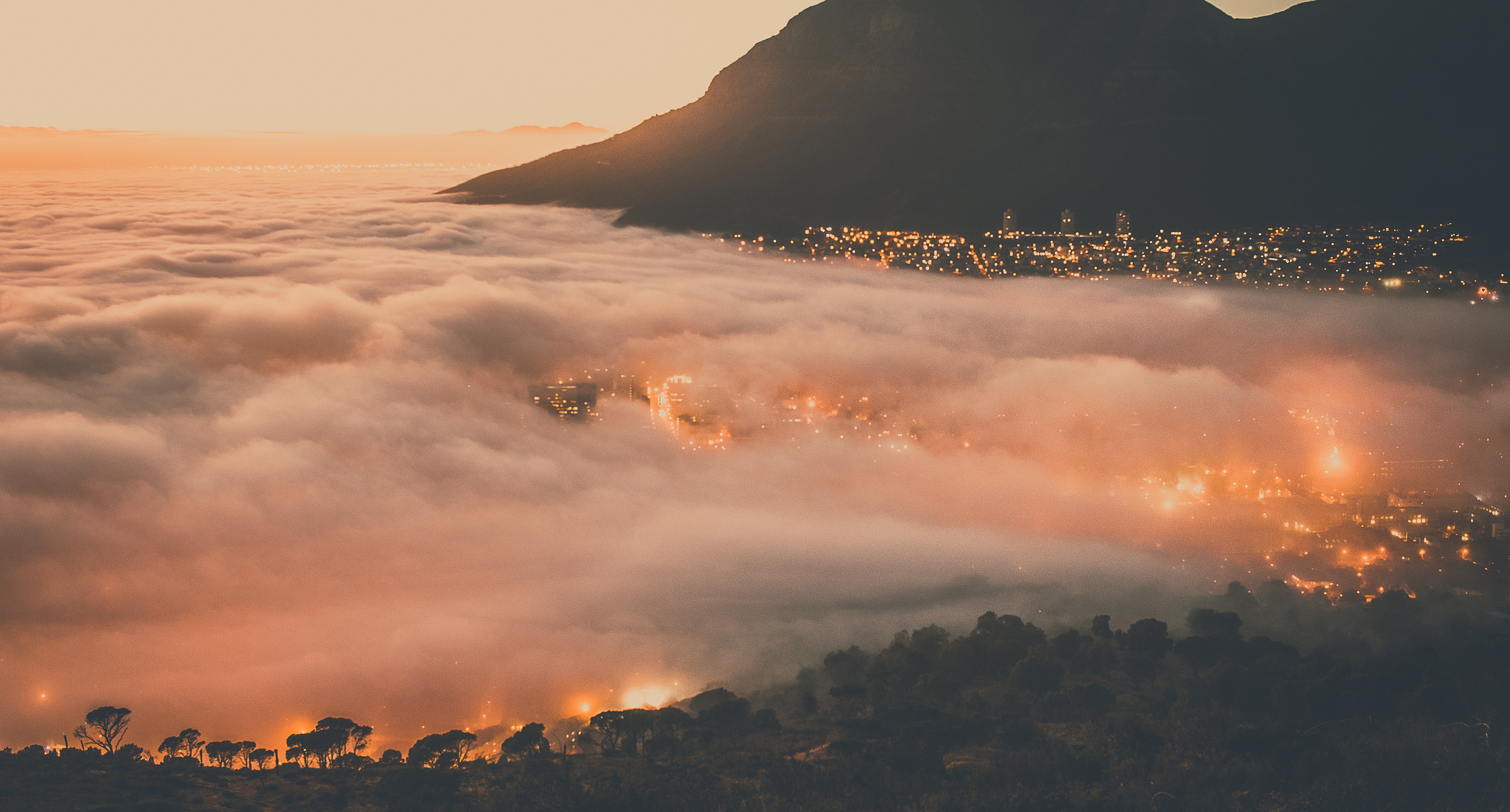 City lights shrouded in fog at sunset with mountain silhouette HD Wallpaper
