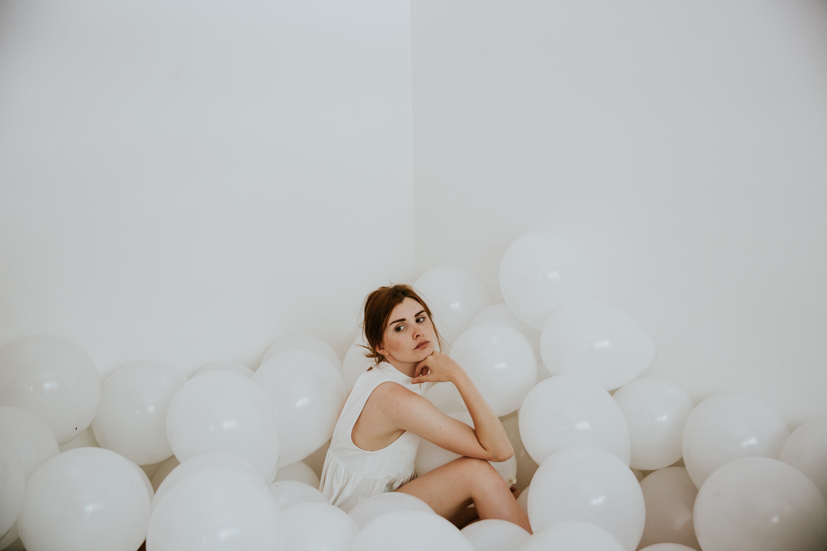 Woman sitting among white balloons in a room HD Wallpaper