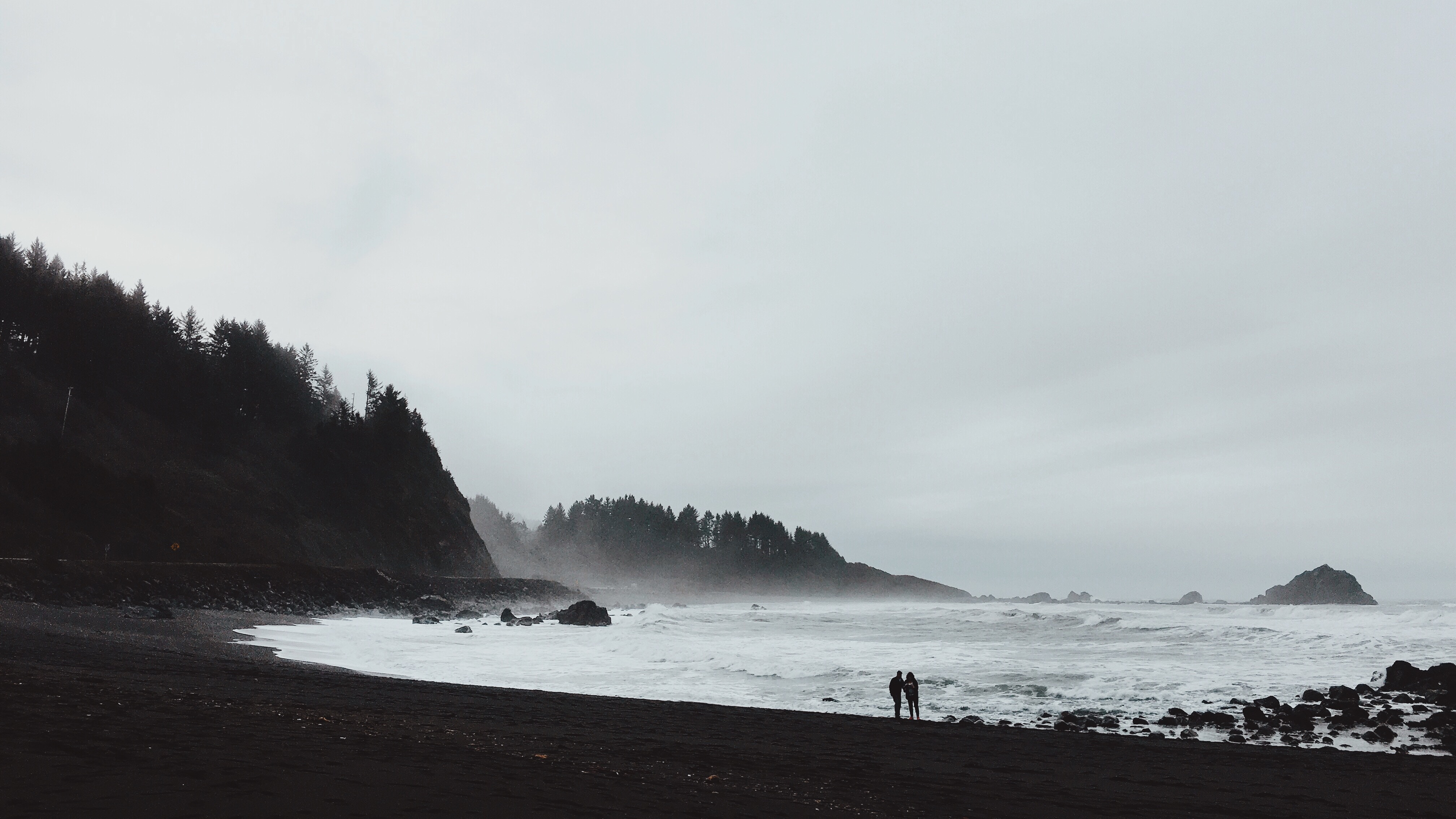 Silhouettes of two people on a foggy beach by the ocean HD Wallpaper