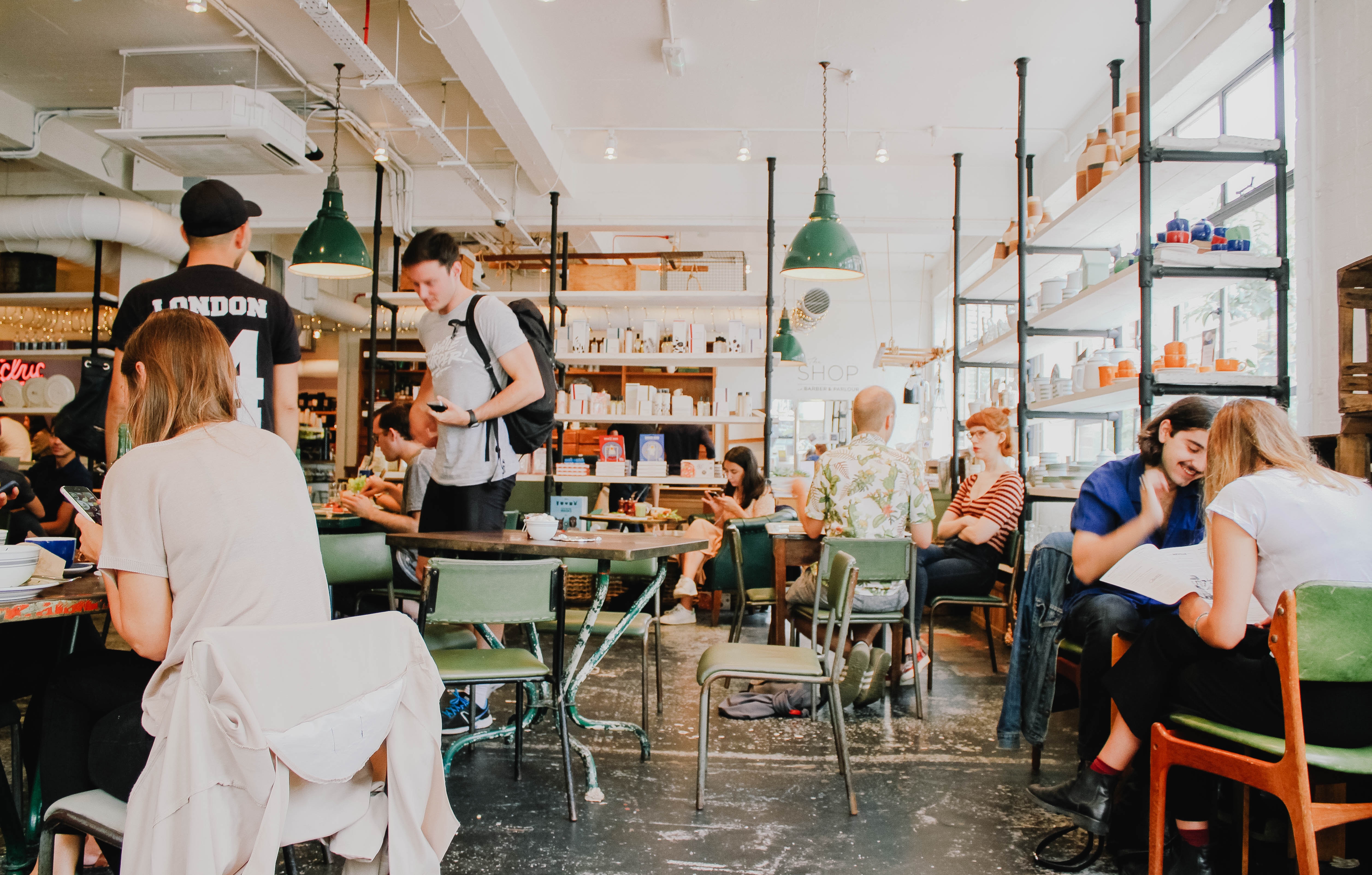 People sitting at tables in a London cafe with shelves HD Wallpaper