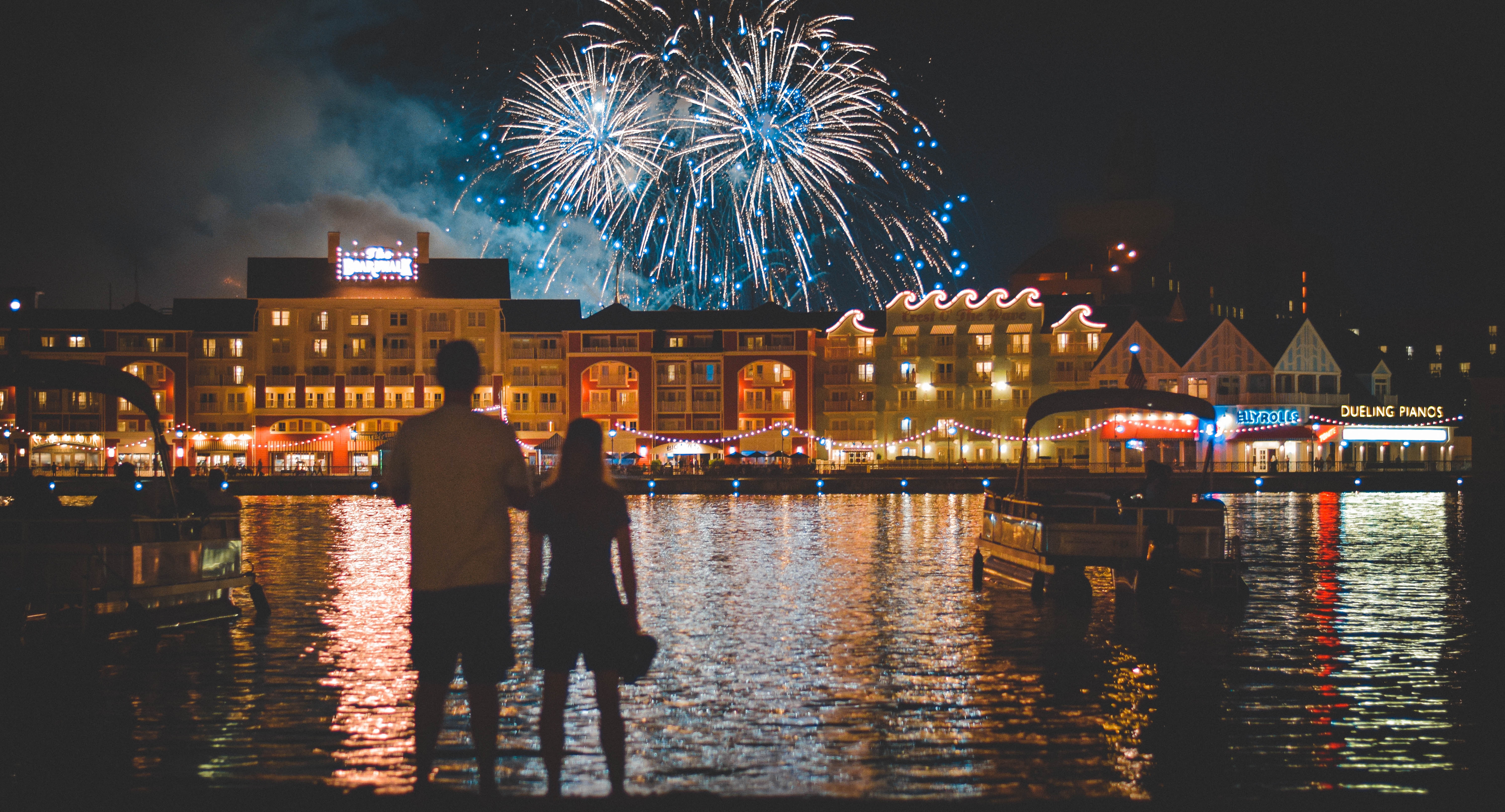 Couple watches fireworks over a waterfront town at night HD Wallpaper