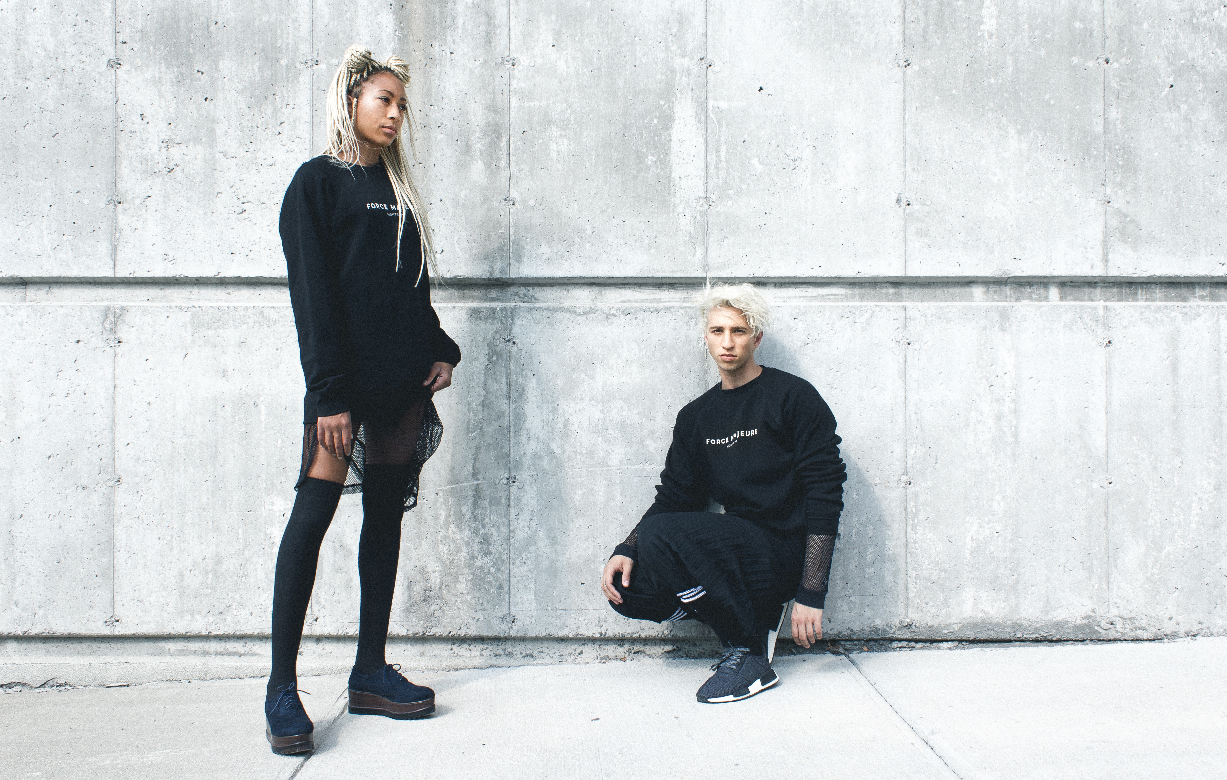 Man and woman in black sweaters against concrete wall HD Wallpaper