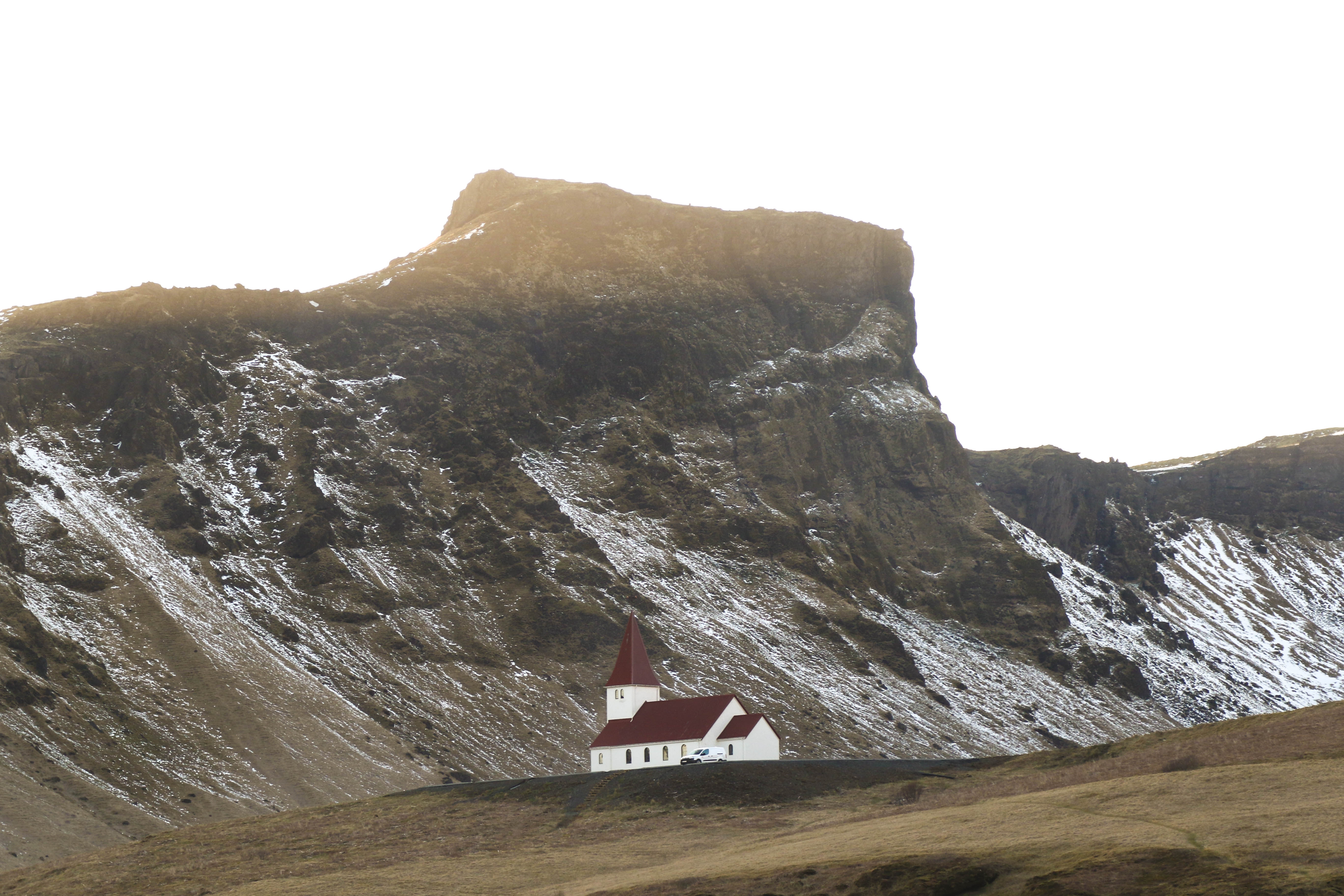 White church with red steeple at the base of a mountain in Iceland HD Wallpaper