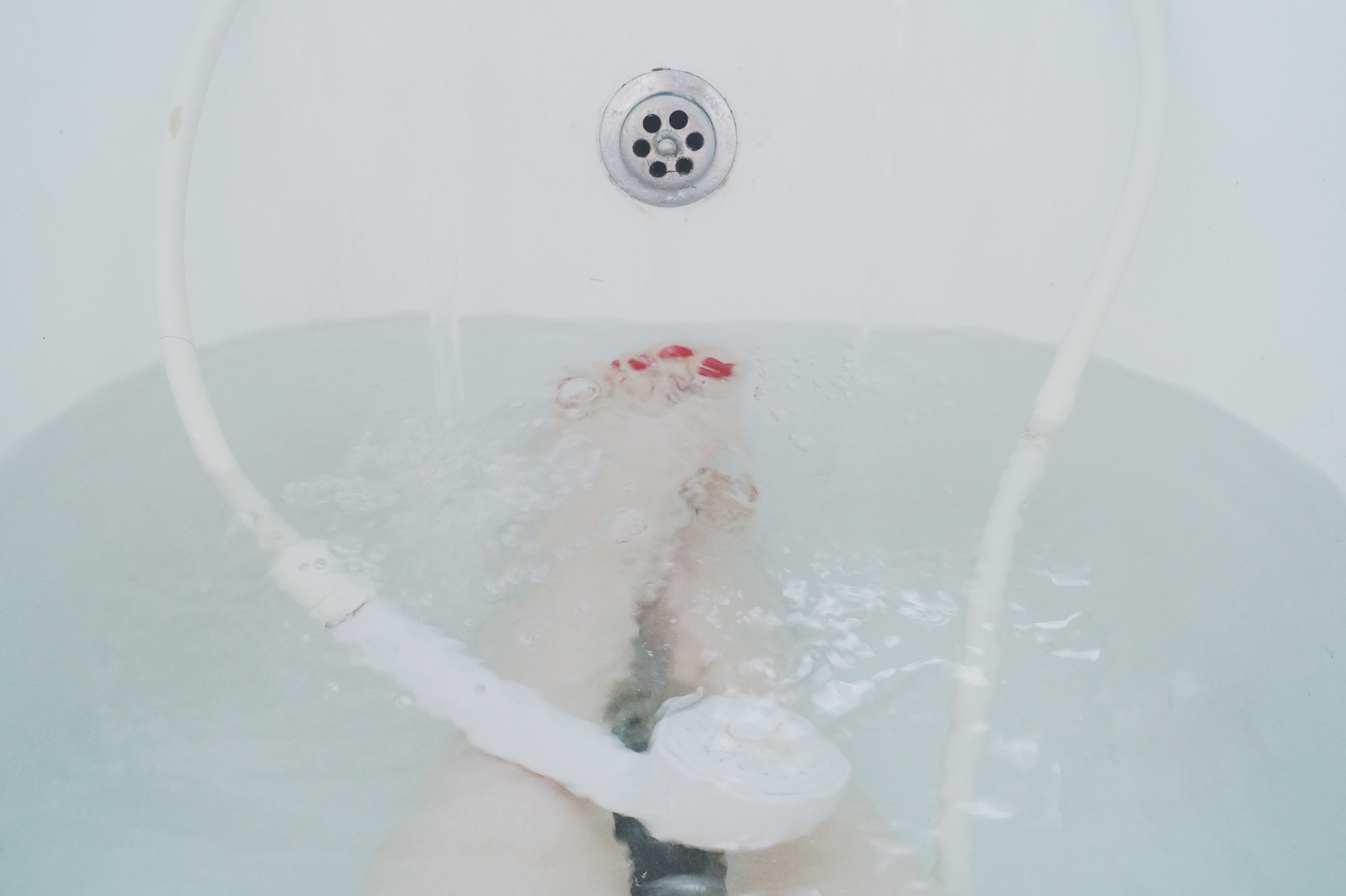 Feet in a bathtub with running water and shower head HD Wallpaper