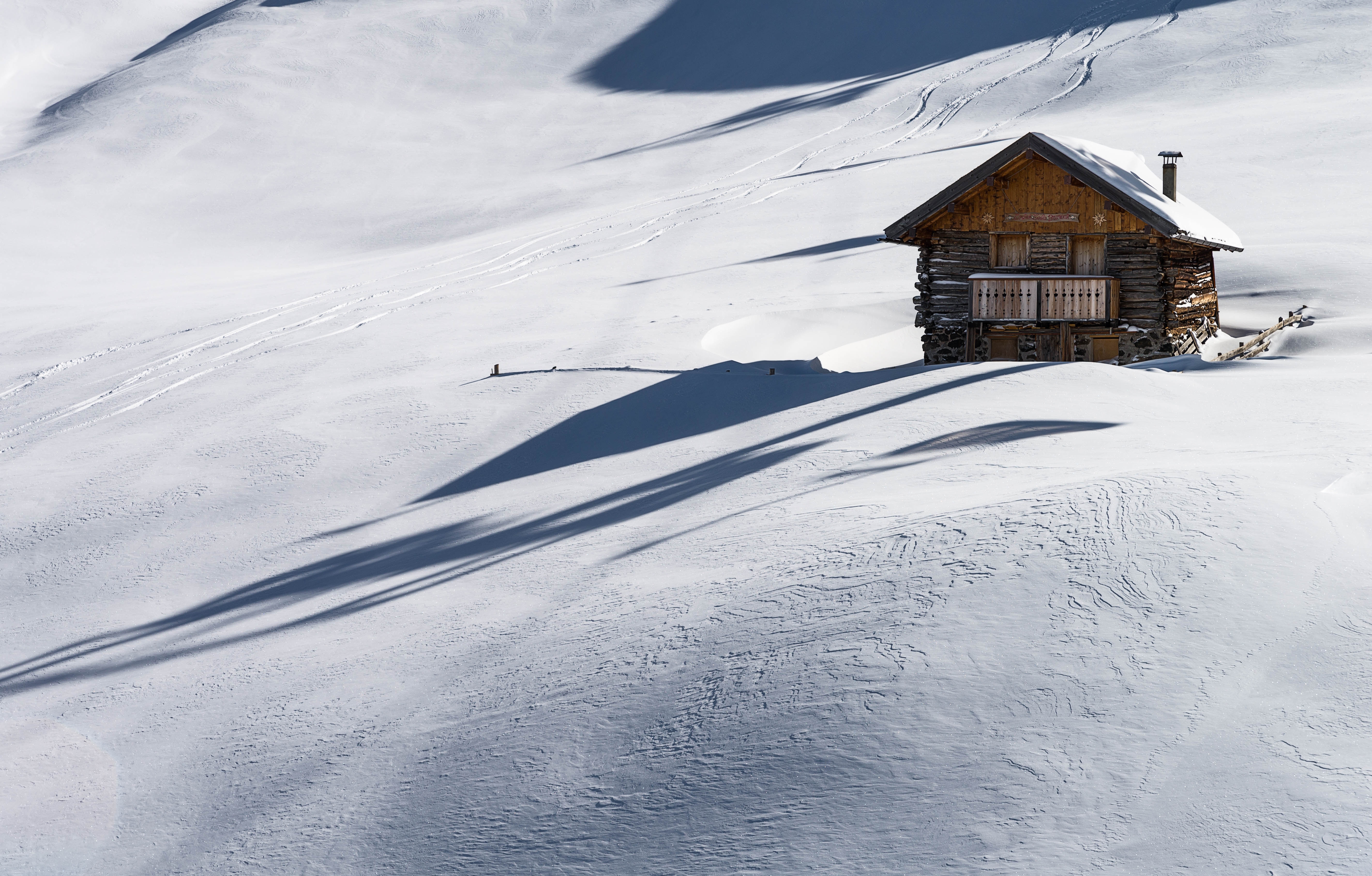 Wooden cabin in a snowy mountain landscape with long shadows HD Wallpaper
