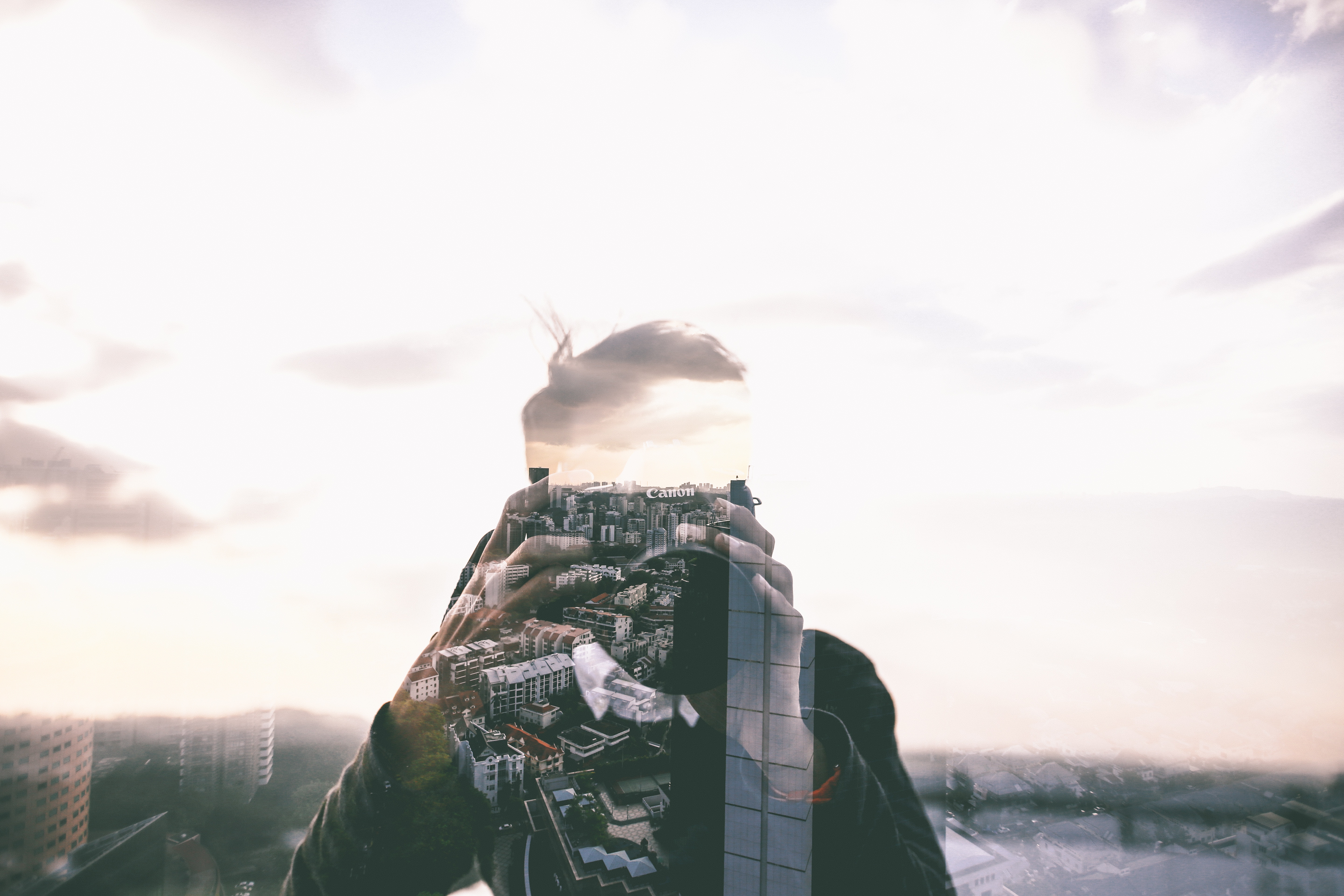 Double exposure of a man holding a Canon camera with a city skyline HD Wallpaper