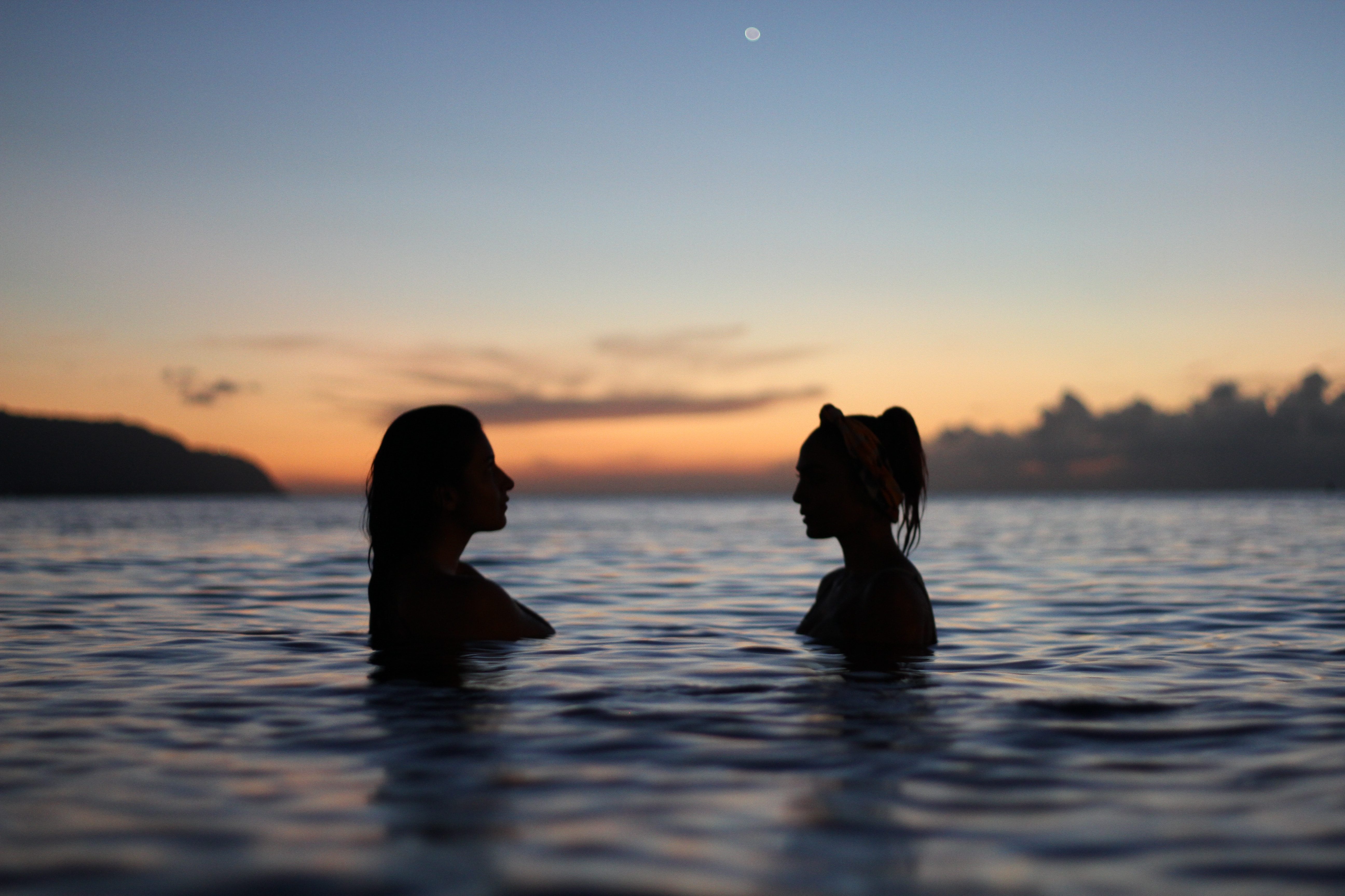 Two women in the ocean at sunset HD Wallpaper