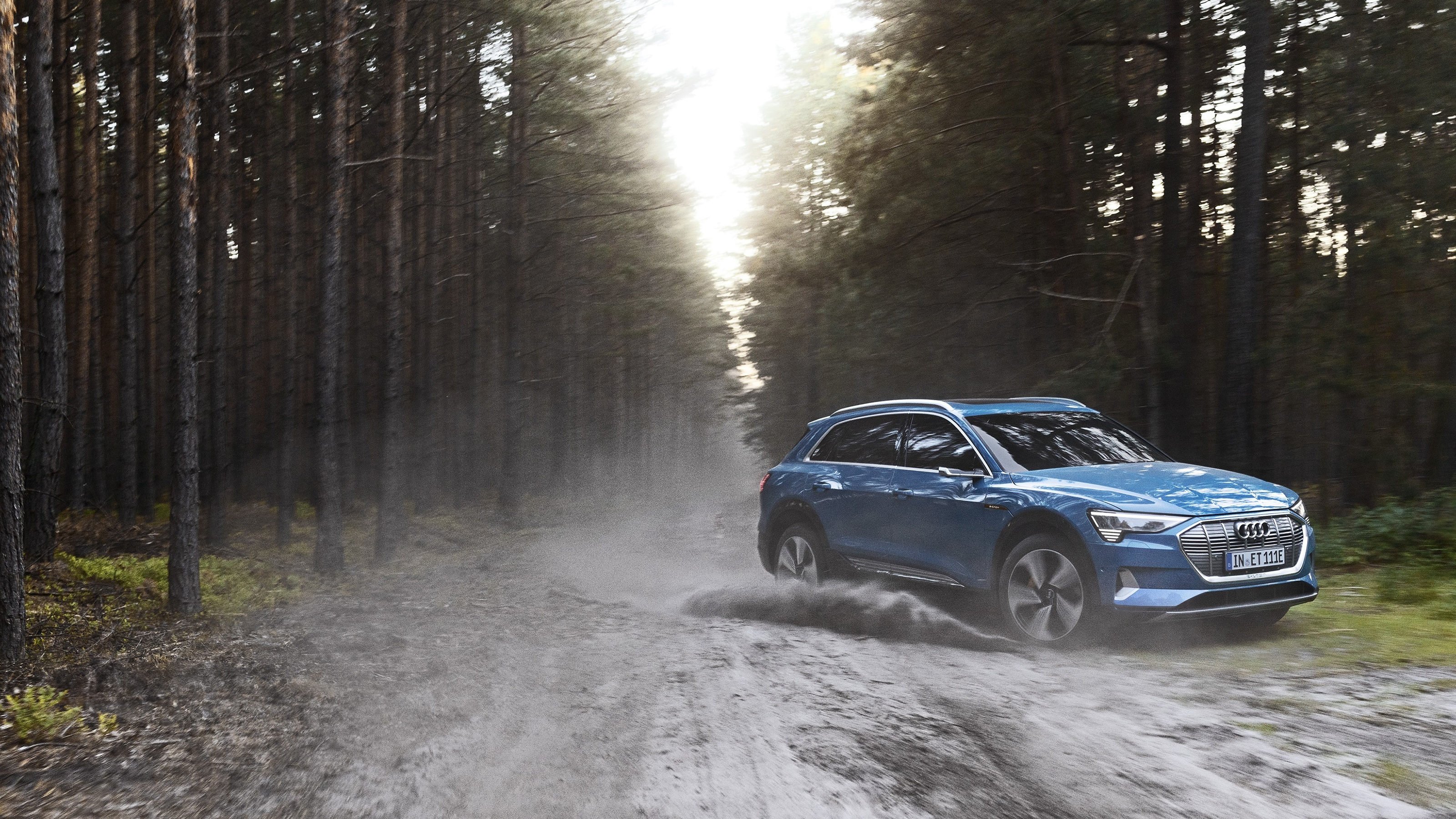 Blue Audi E-tron Quattro driving on a dirt road in a forest HD Wallpaper