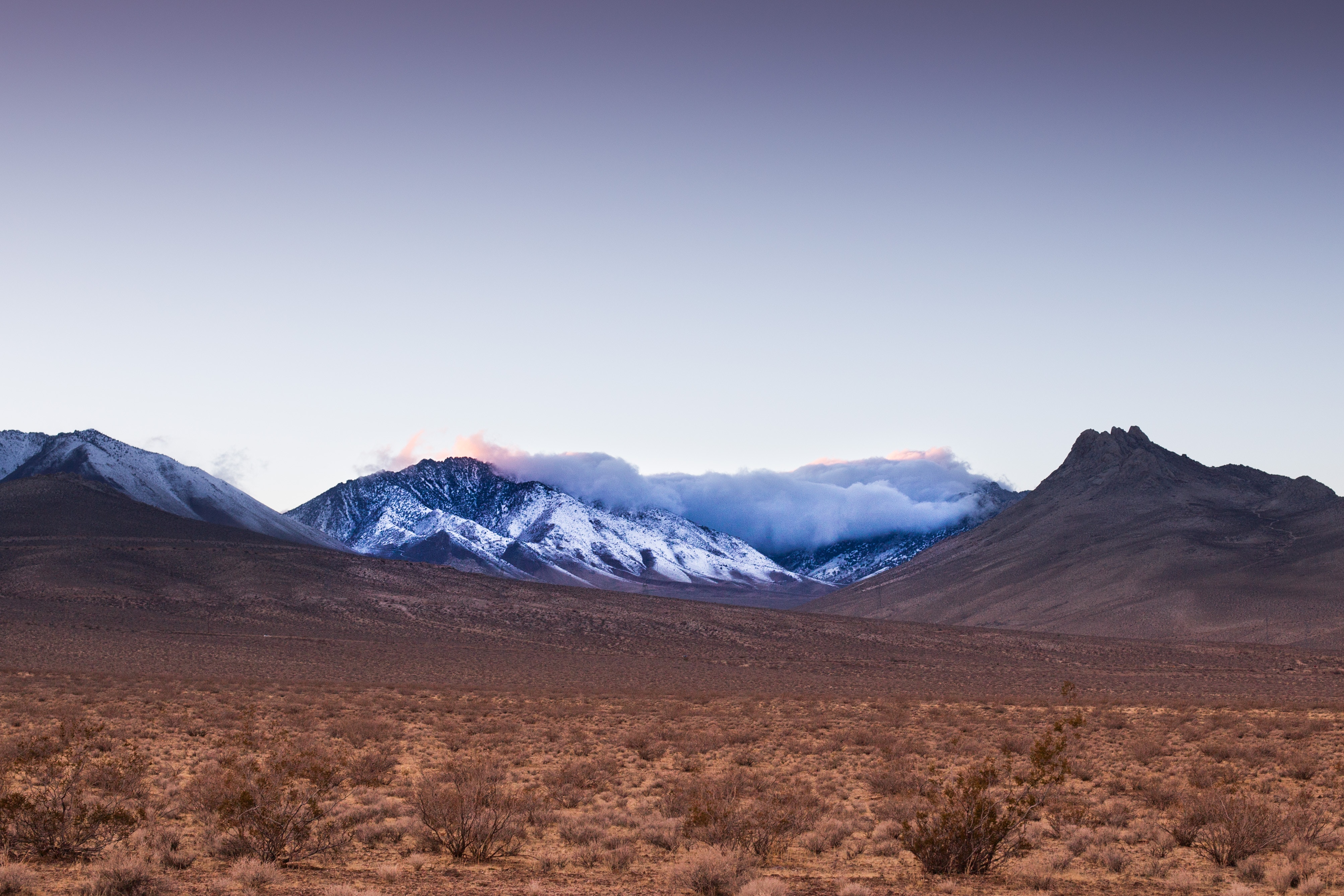Snow-capped mountains at dusk over a desert plain HD Wallpaper