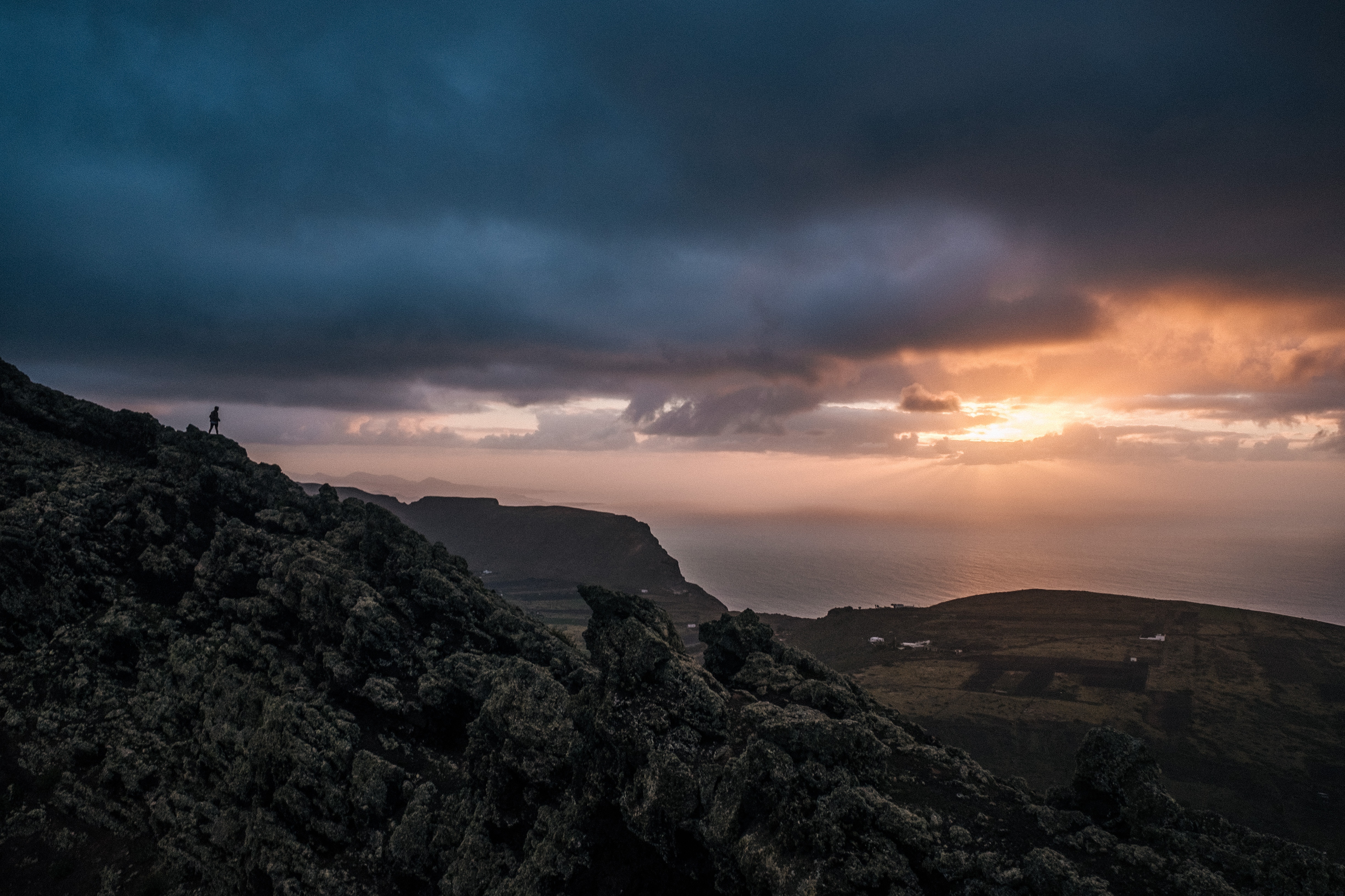 Man on rocky cliff overlooking ocean at sunset HD Wallpaper