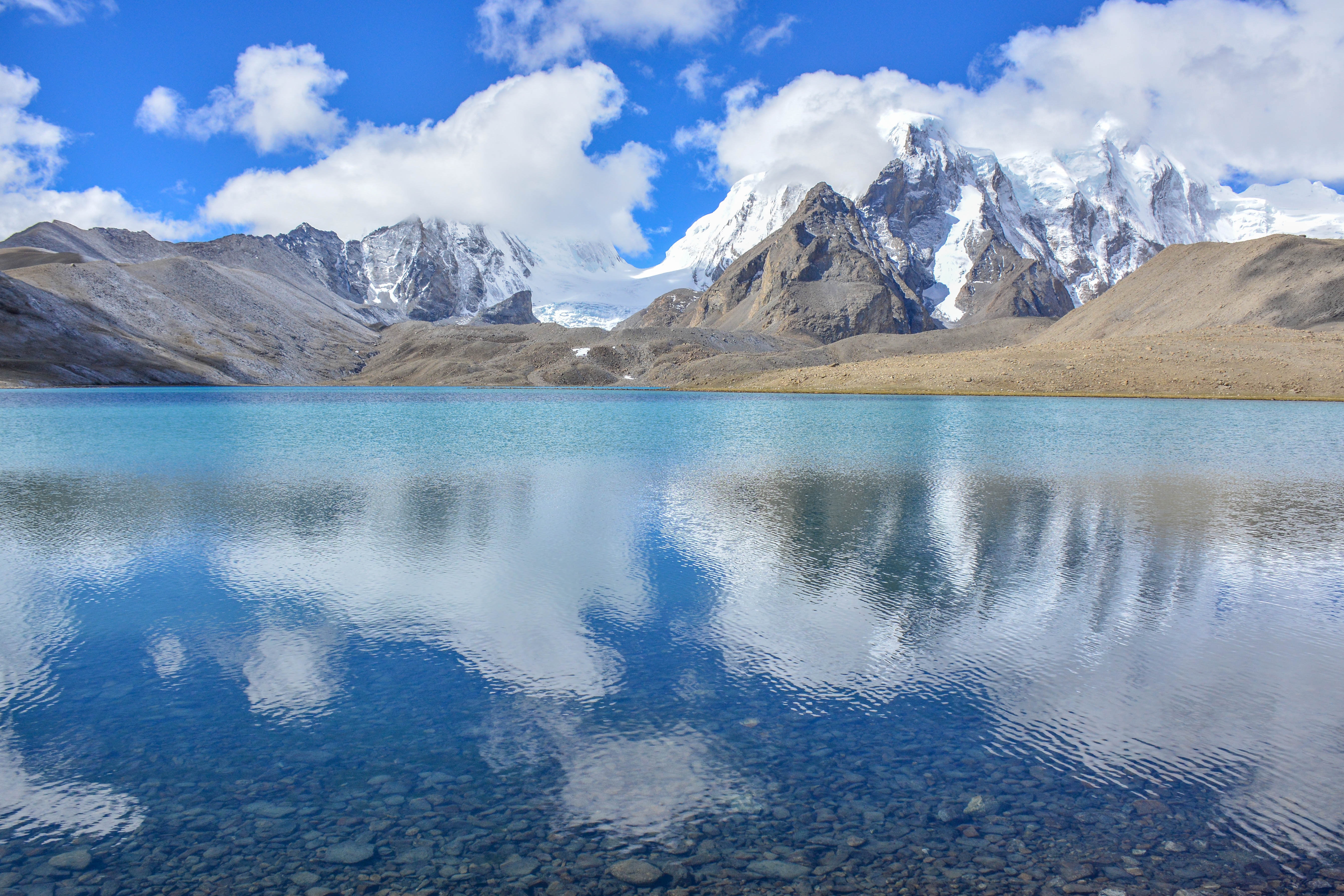 Turquoise lake reflecting snow-capped mountains under a cloudy sky HD Wallpaper