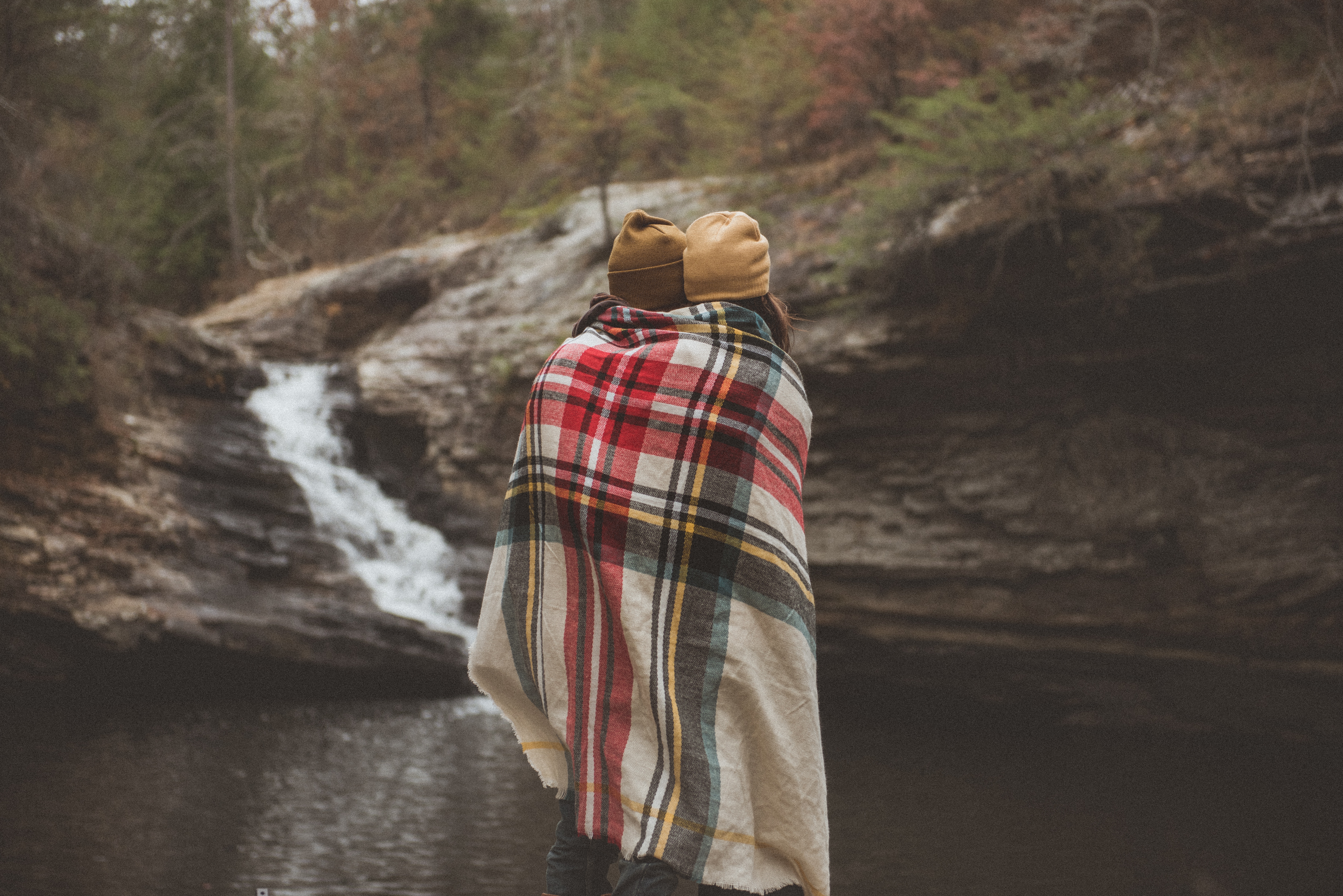 Couple wrapped in blanket by waterfall HD Wallpaper