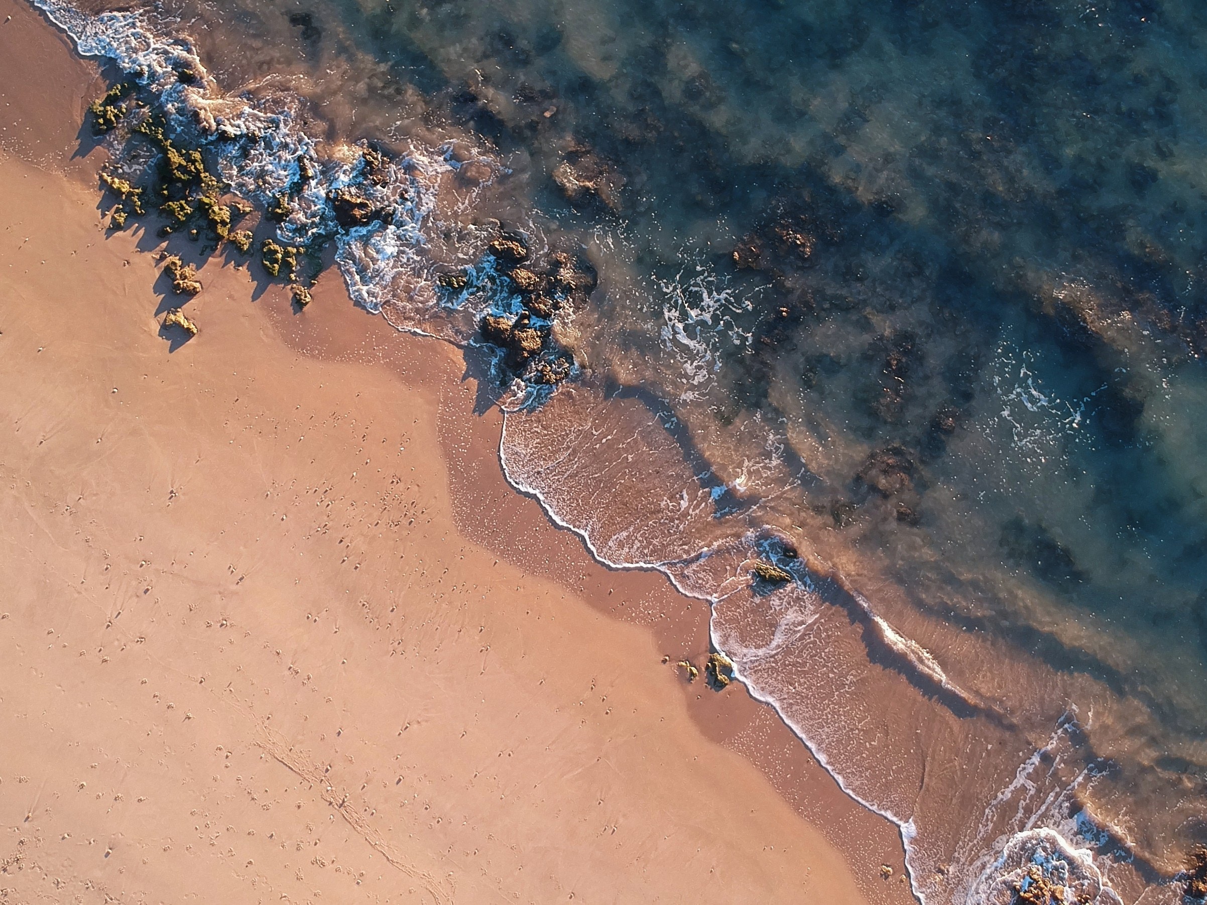 Aerial view of a sandy beach with waves and rocks HD Wallpaper