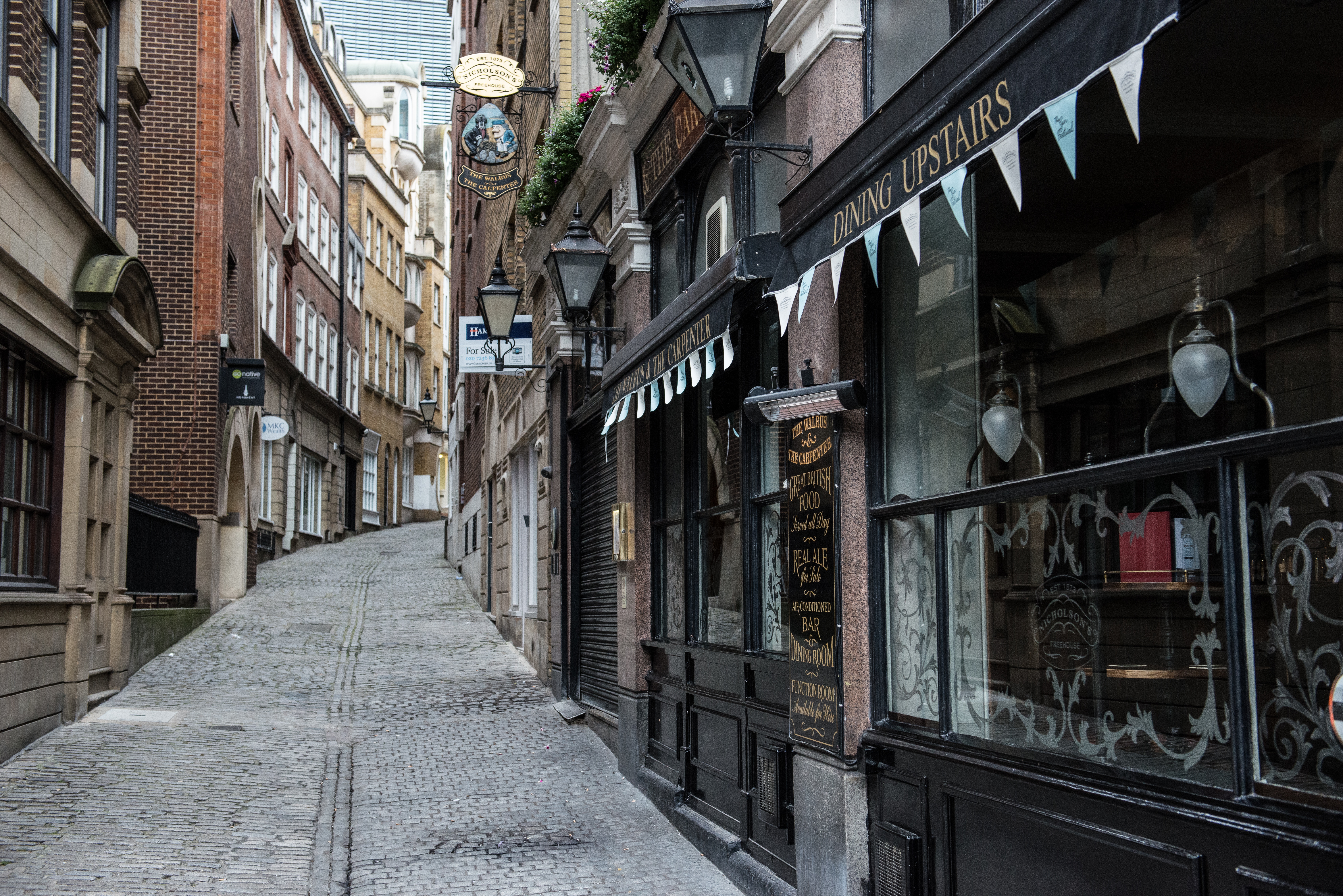 Narrow cobblestone street with shops and buildings HD Wallpaper