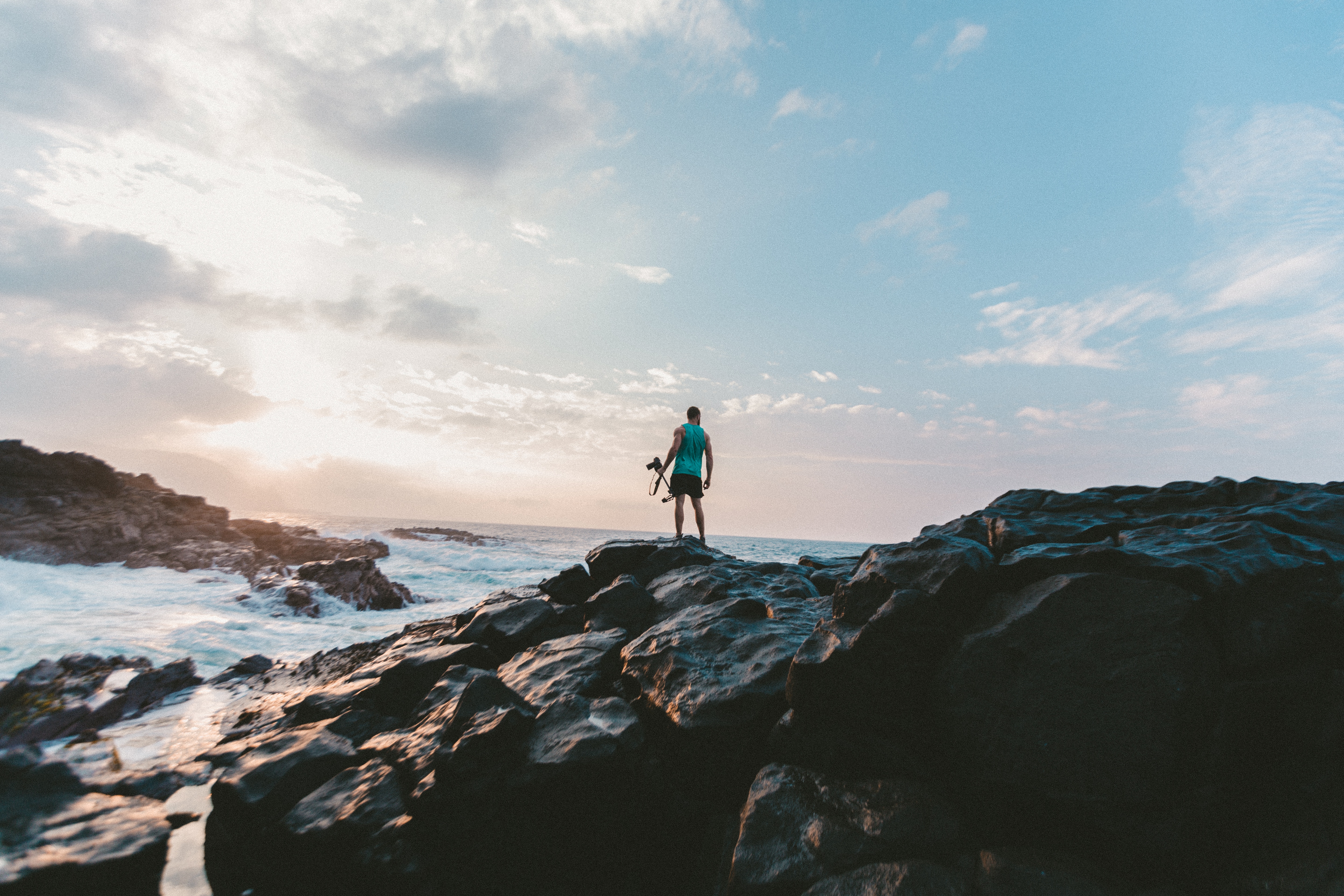 Man with camera standing on rocks by the sea HD Wallpaper