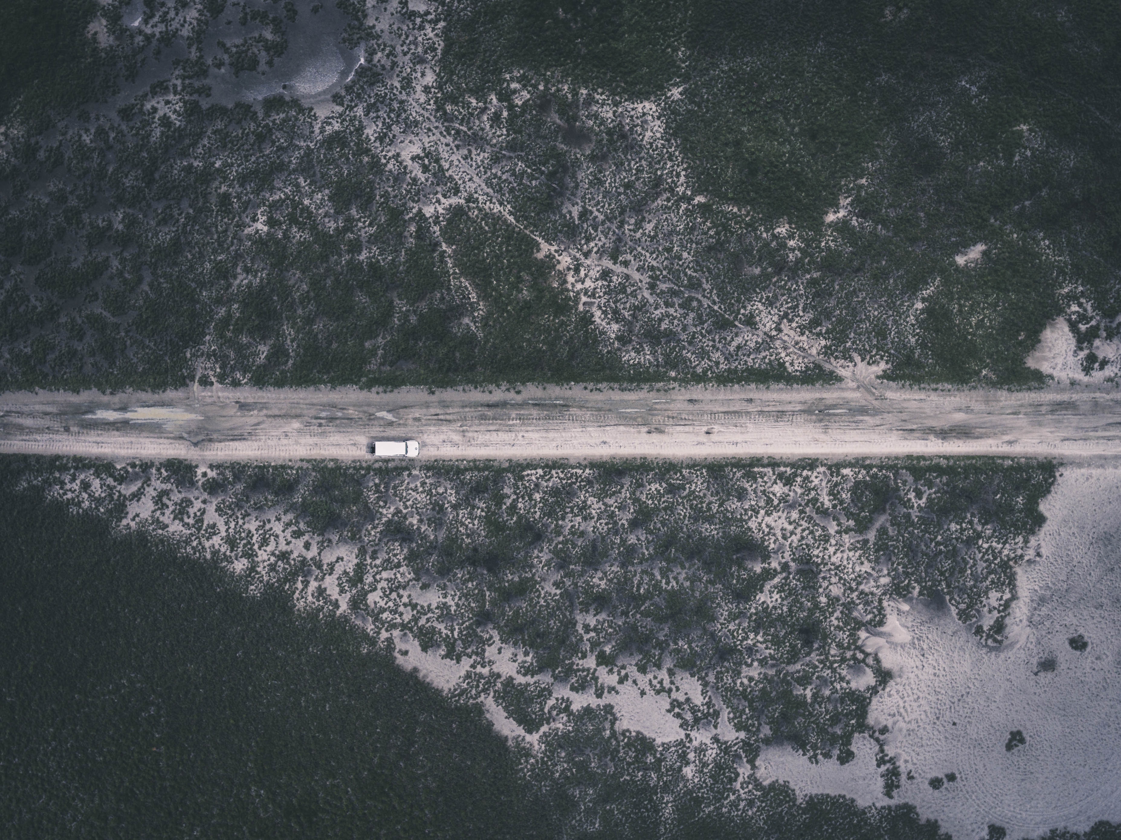 Aerial view of a white van on a dirt road through a desolate landscape HD Wallpaper