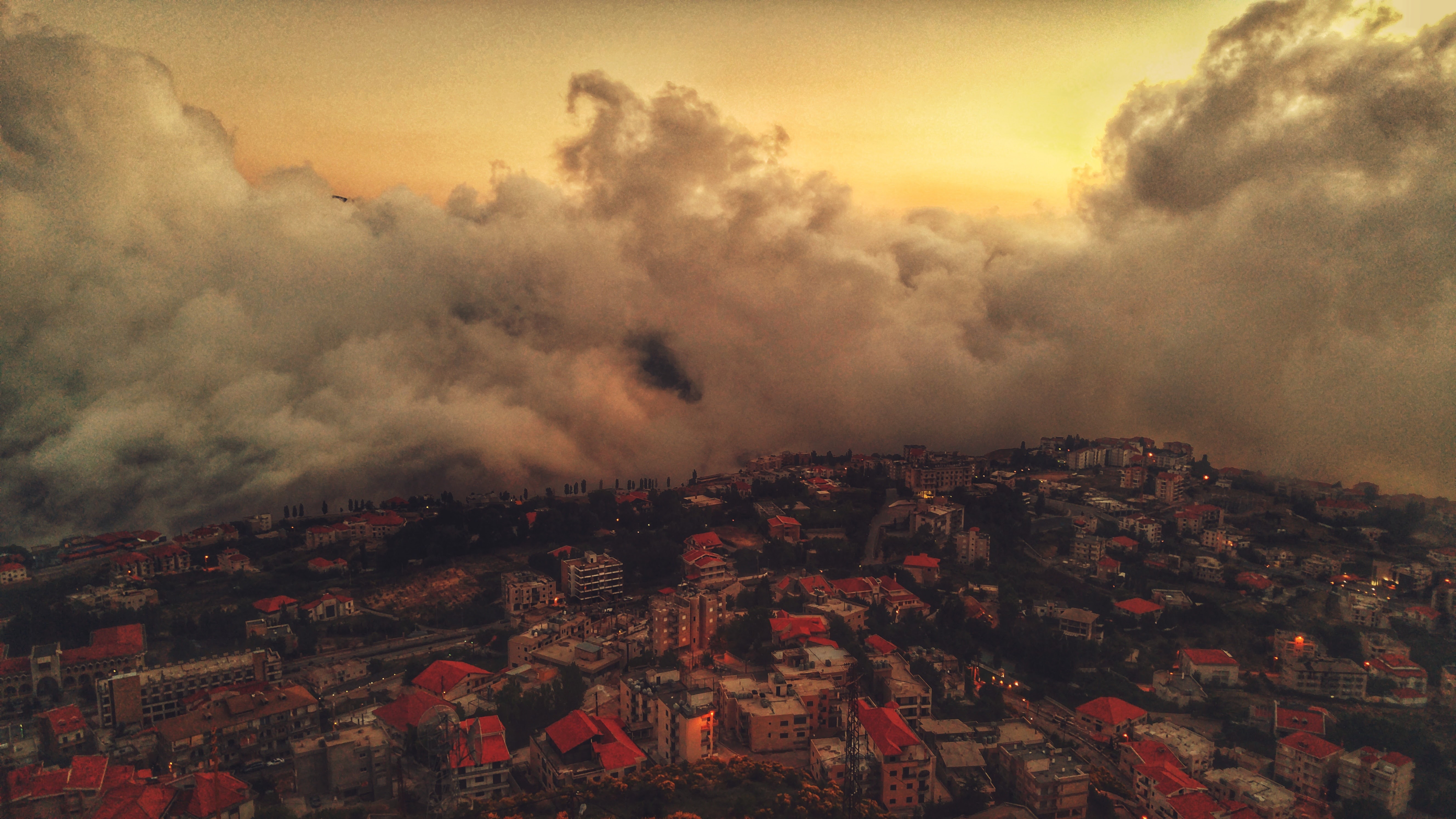 Cityscape with red roofs under dramatic clouds at sunset HD Wallpaper