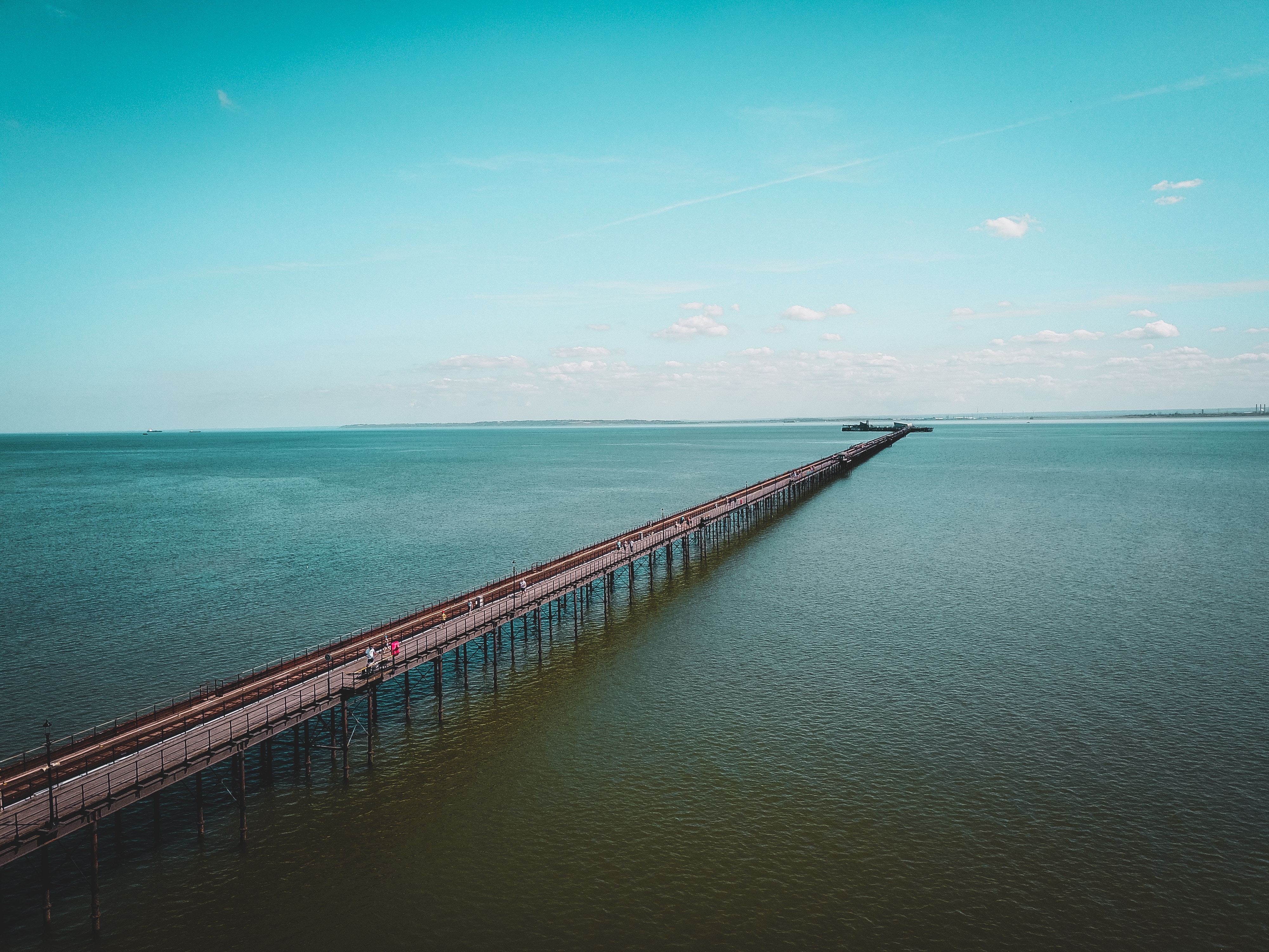 Long pier extending over the sea under a blue sky HD Wallpaper