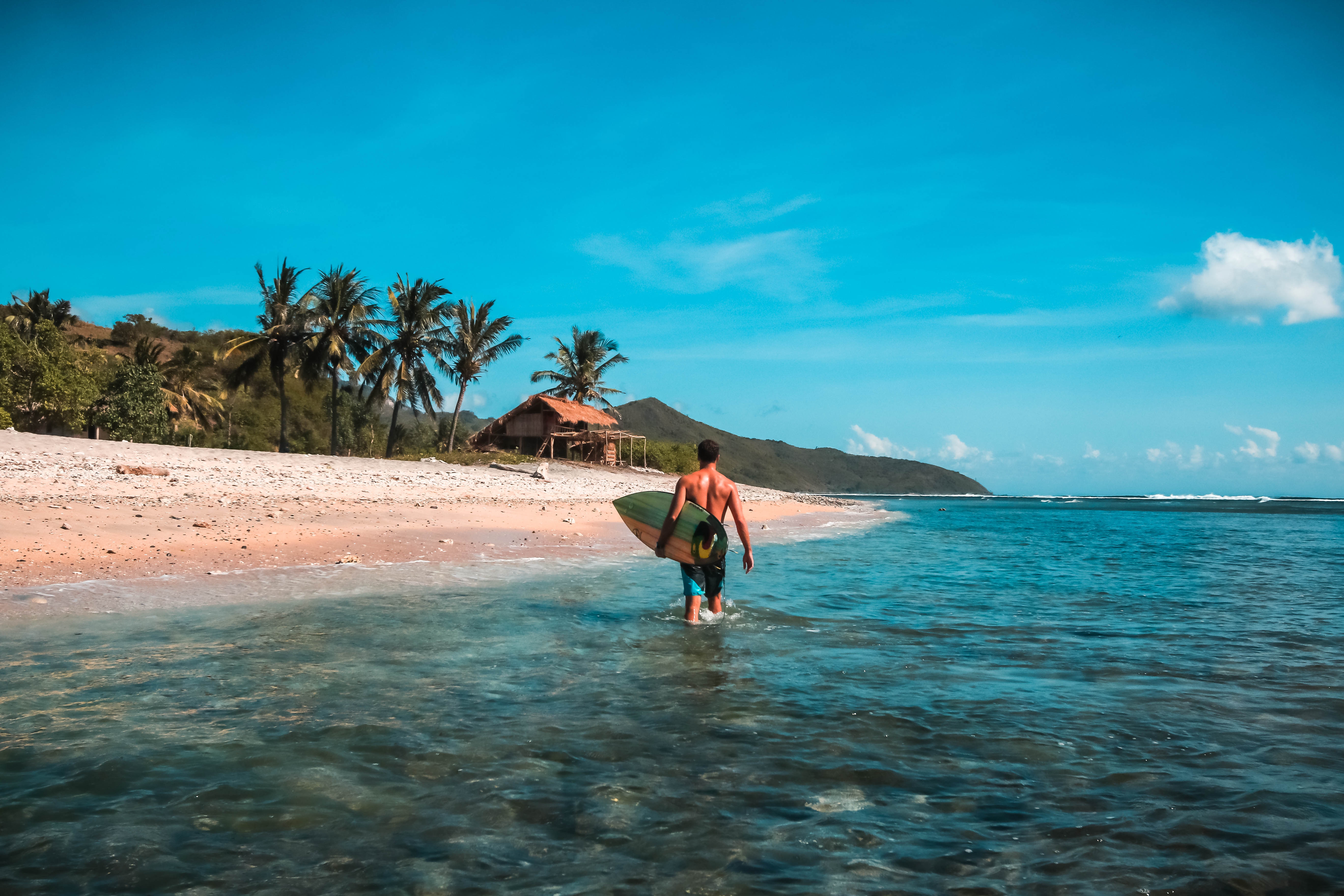 Man with surfboard walks into the ocean in Indonesia HD Wallpaper