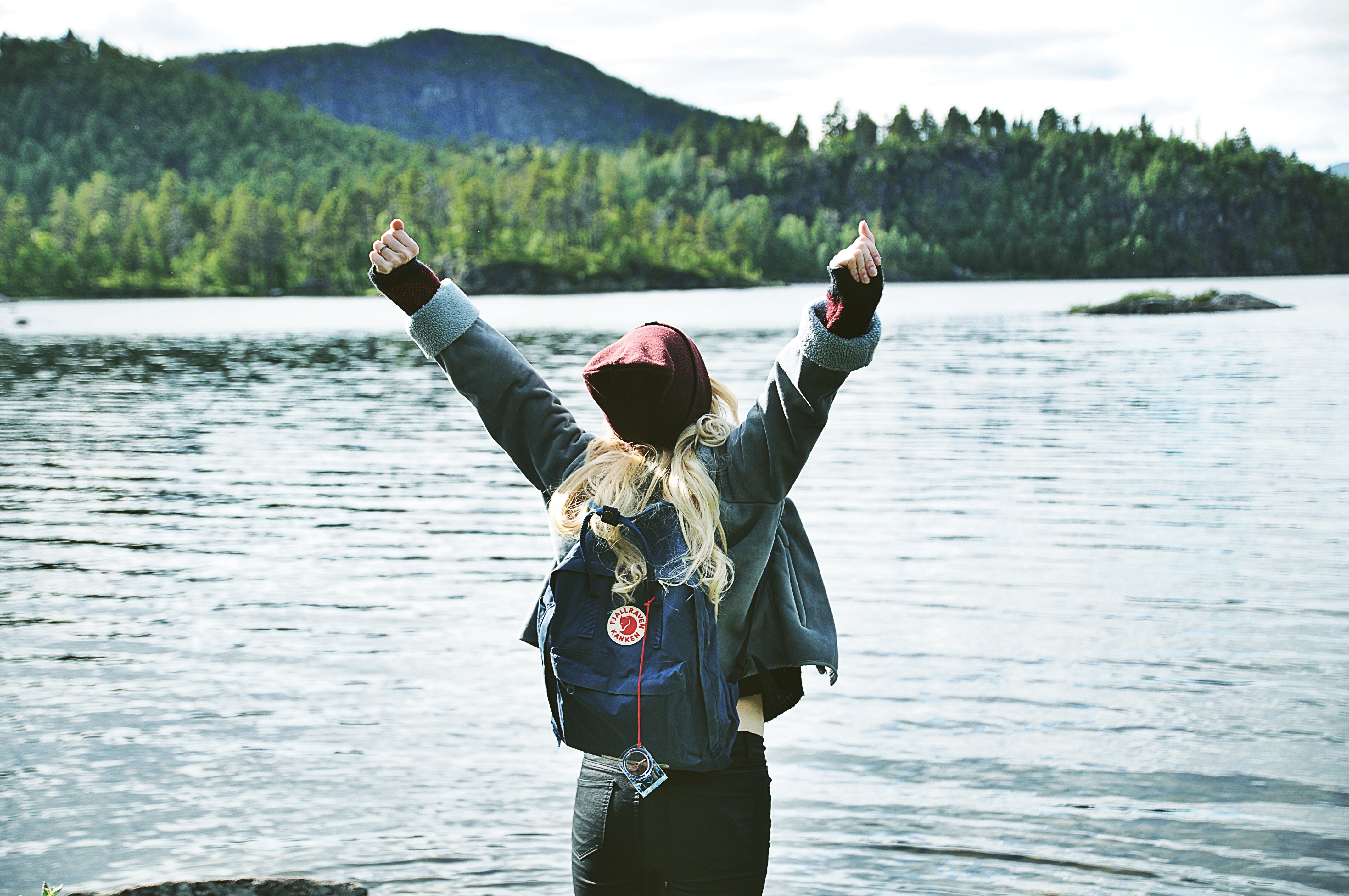 Woman with backpack celebrating by a lake HD Wallpaper