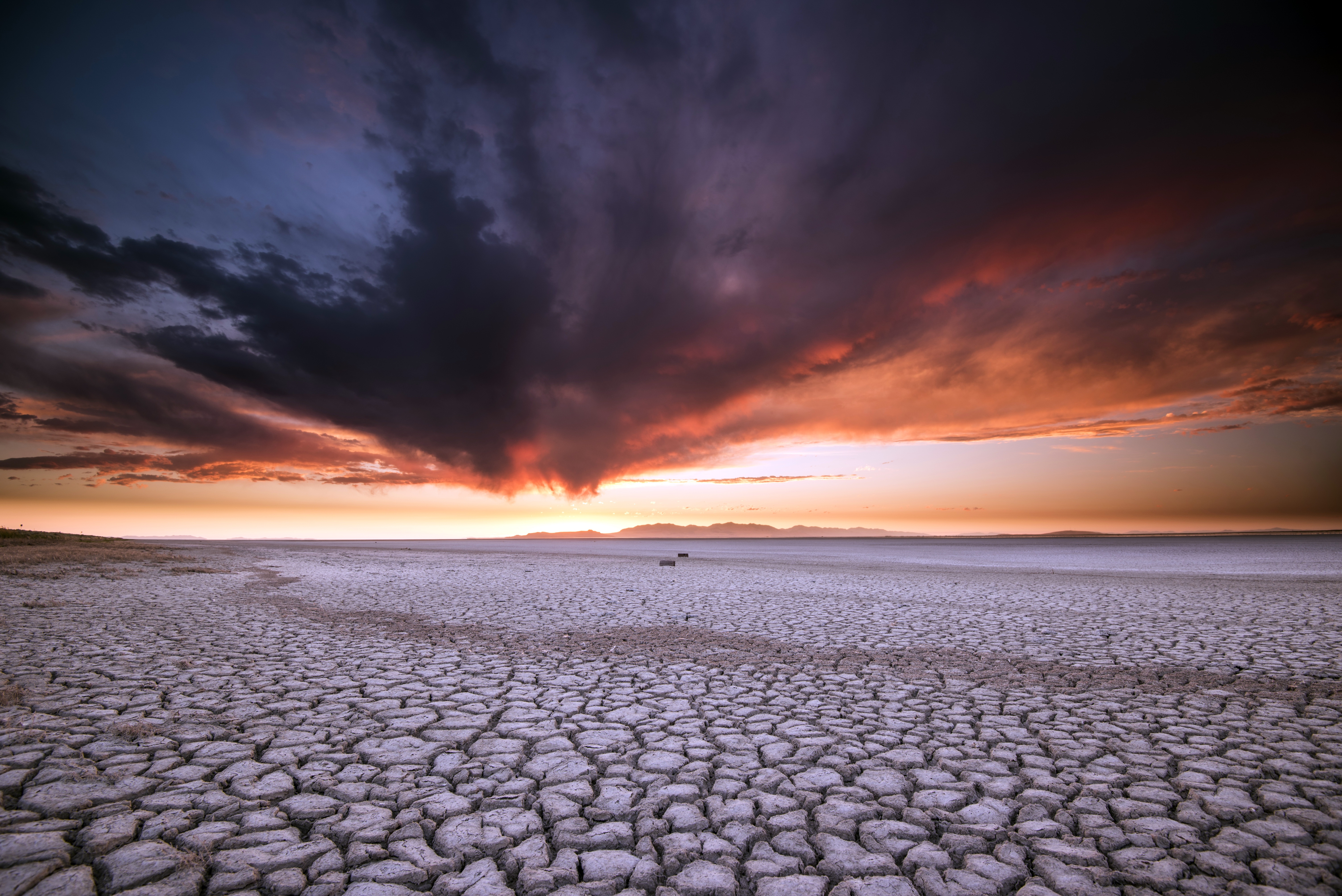 Cracked desert landscape under a dramatic sunset sky HD Wallpaper