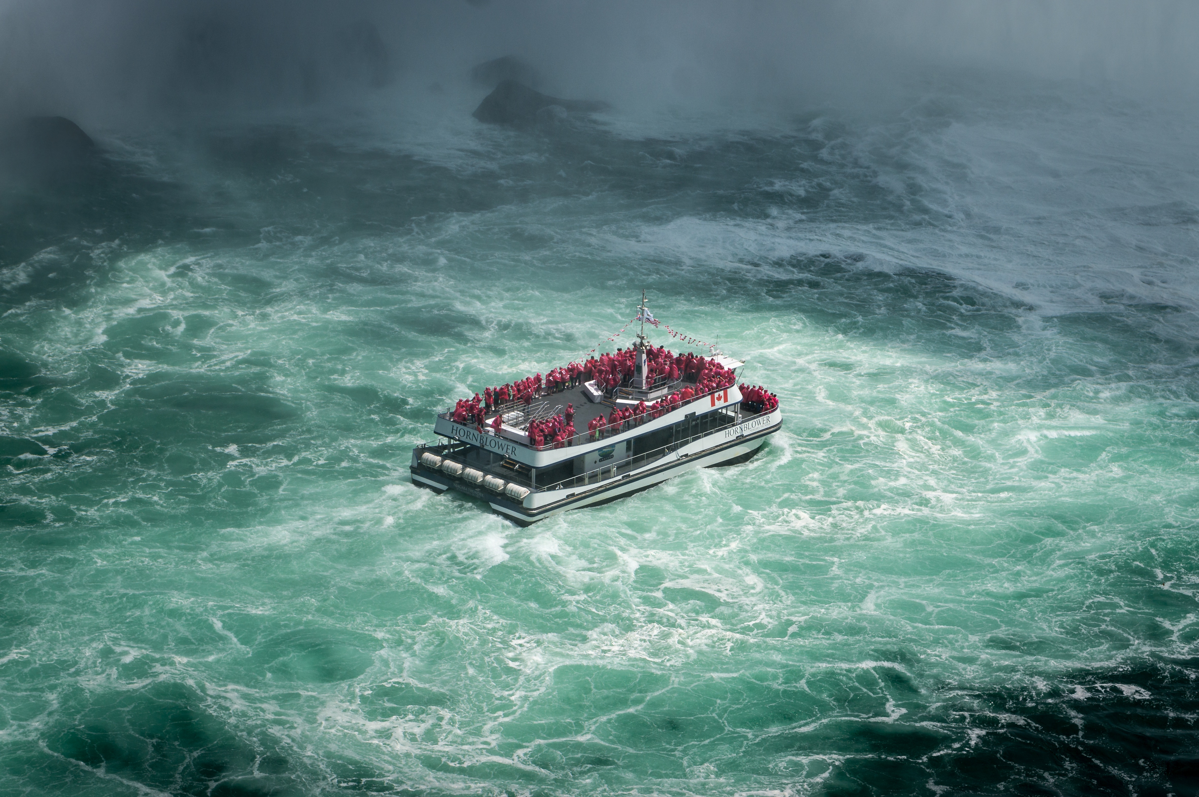 Tour boat navigating turbulent waters near a waterfall HD Wallpaper