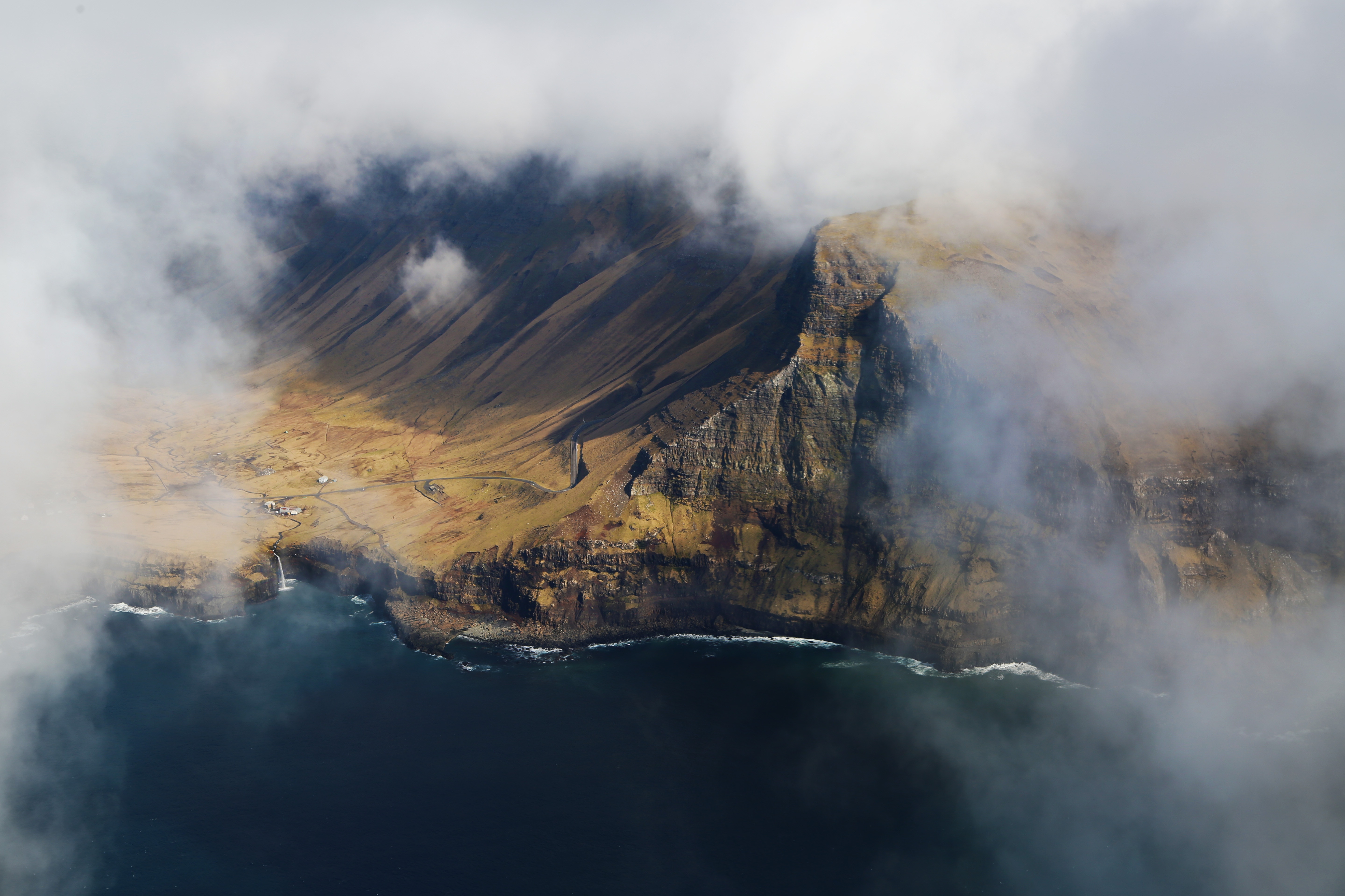 Aerial view of a misty coastline with a waterfall and mountains HD Wallpaper