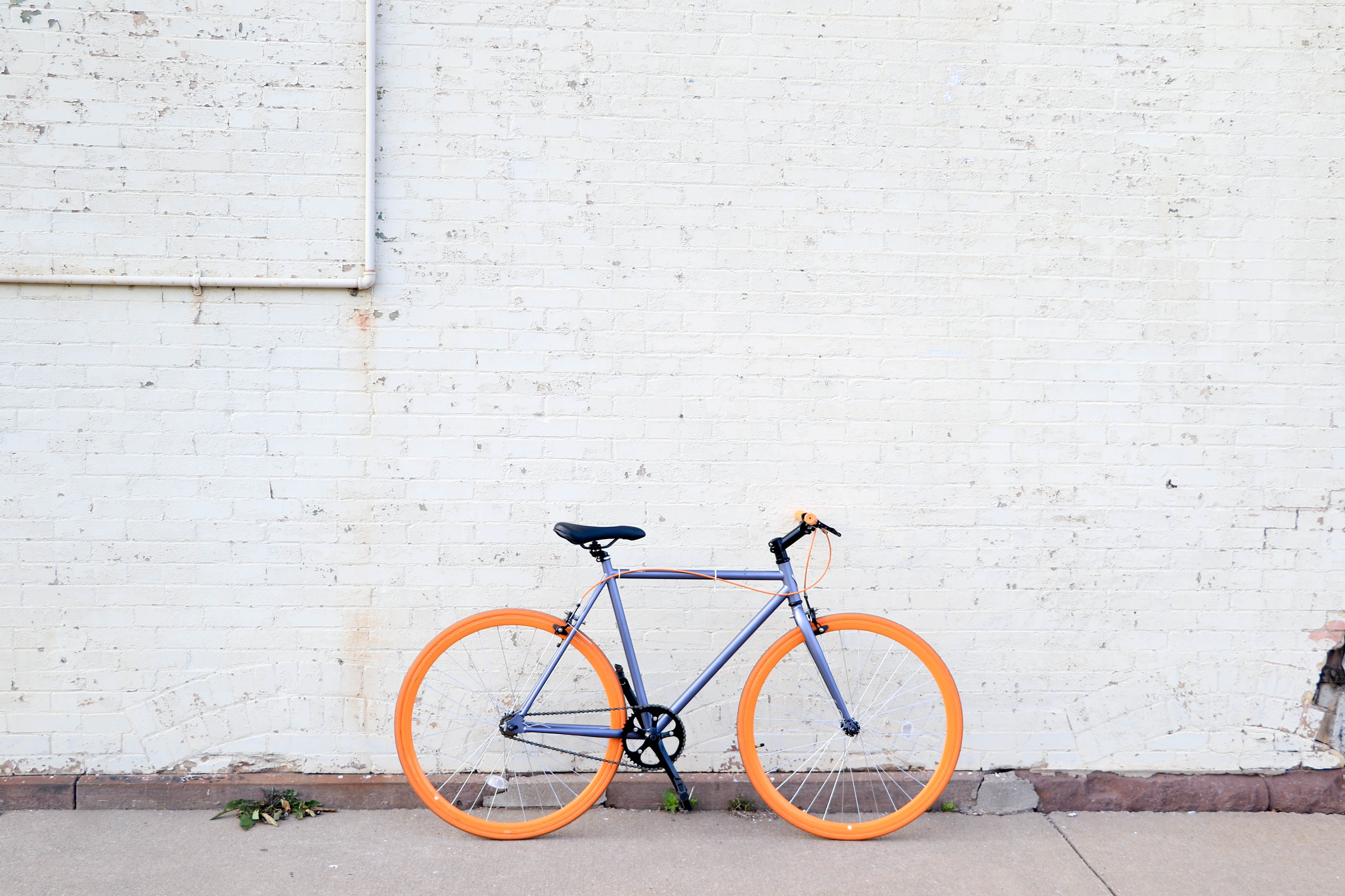 Purple fixed-wheel bicycle with orange wheels parked against a white brick wall HD Wallpaper