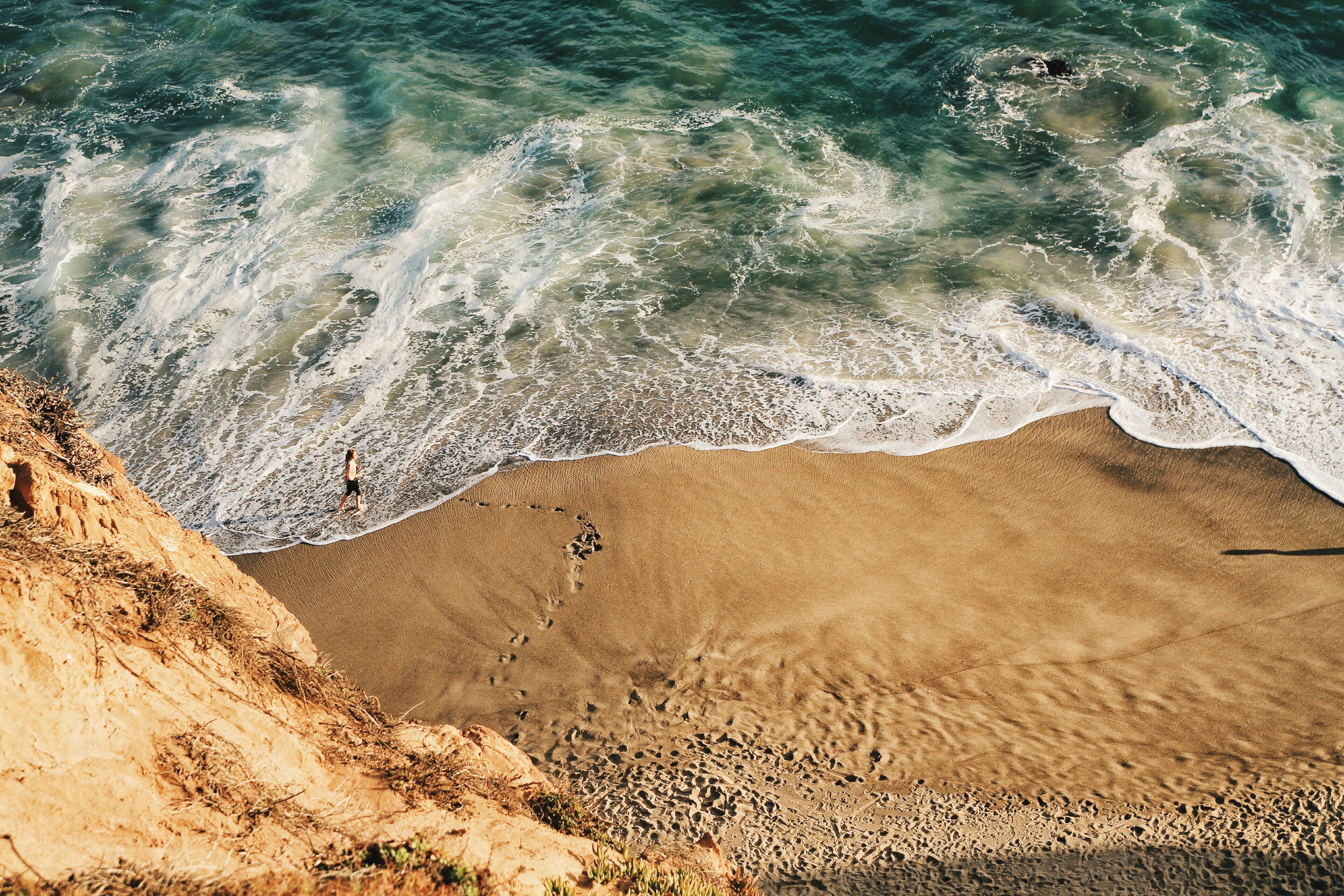 Person walking on a sandy beach by the ocean HD Wallpaper