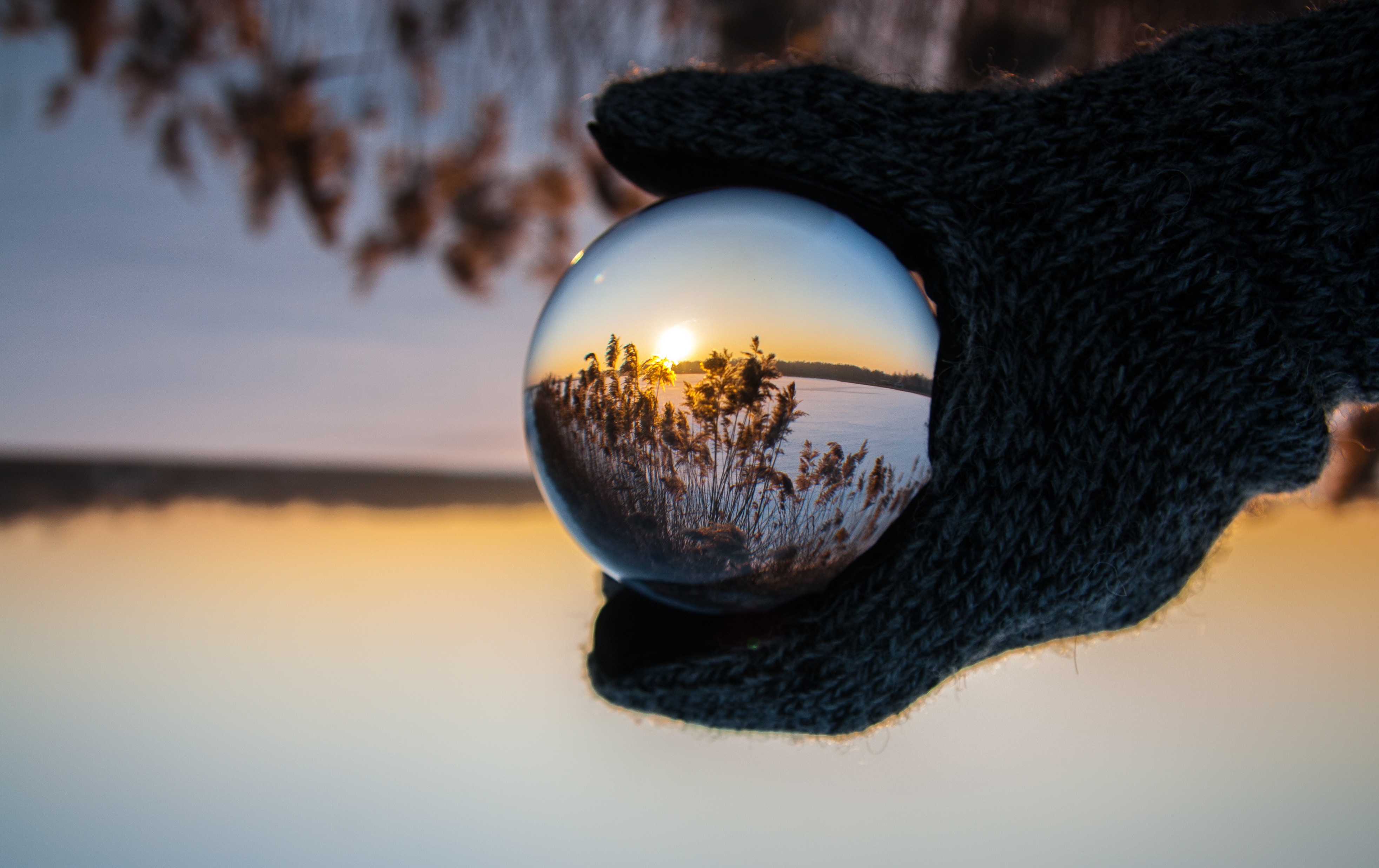 Gloved hand holding a glass ball reflecting a winter sunrise HD Wallpaper