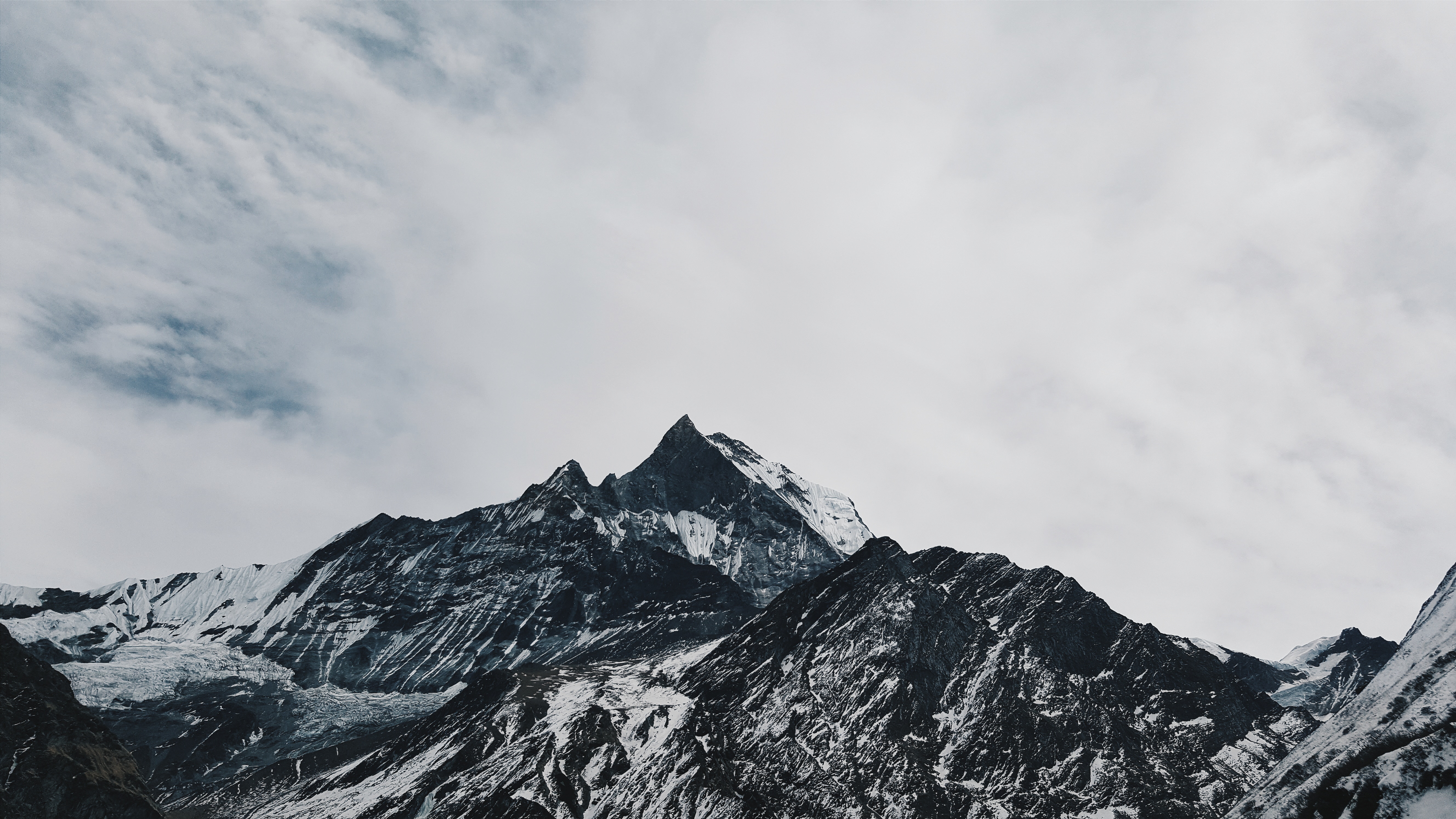 Snow-covered mountain range under a cloudy sky HD Wallpaper