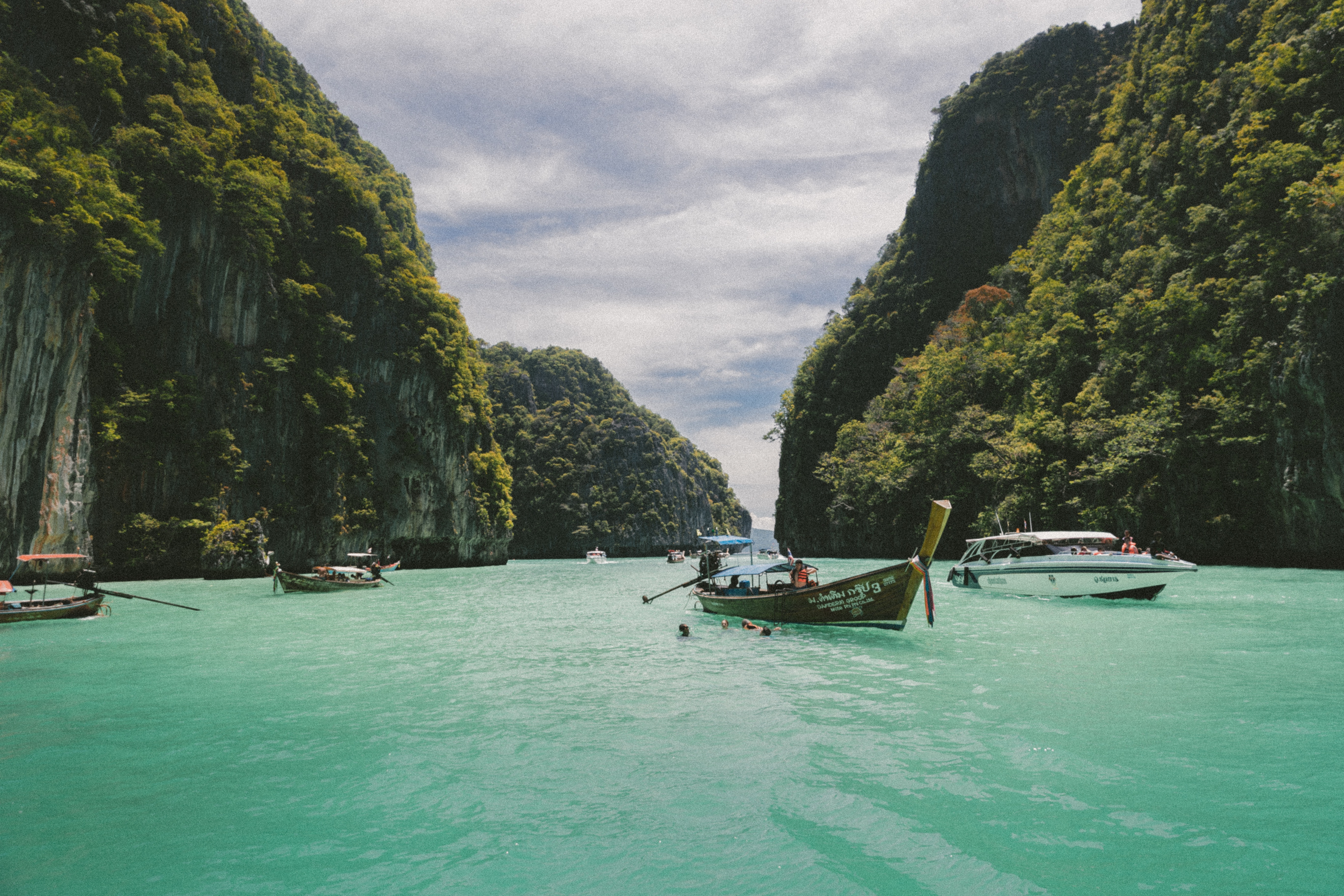 Boats in a turquoise bay surrounded by lush green cliffs HD Wallpaper